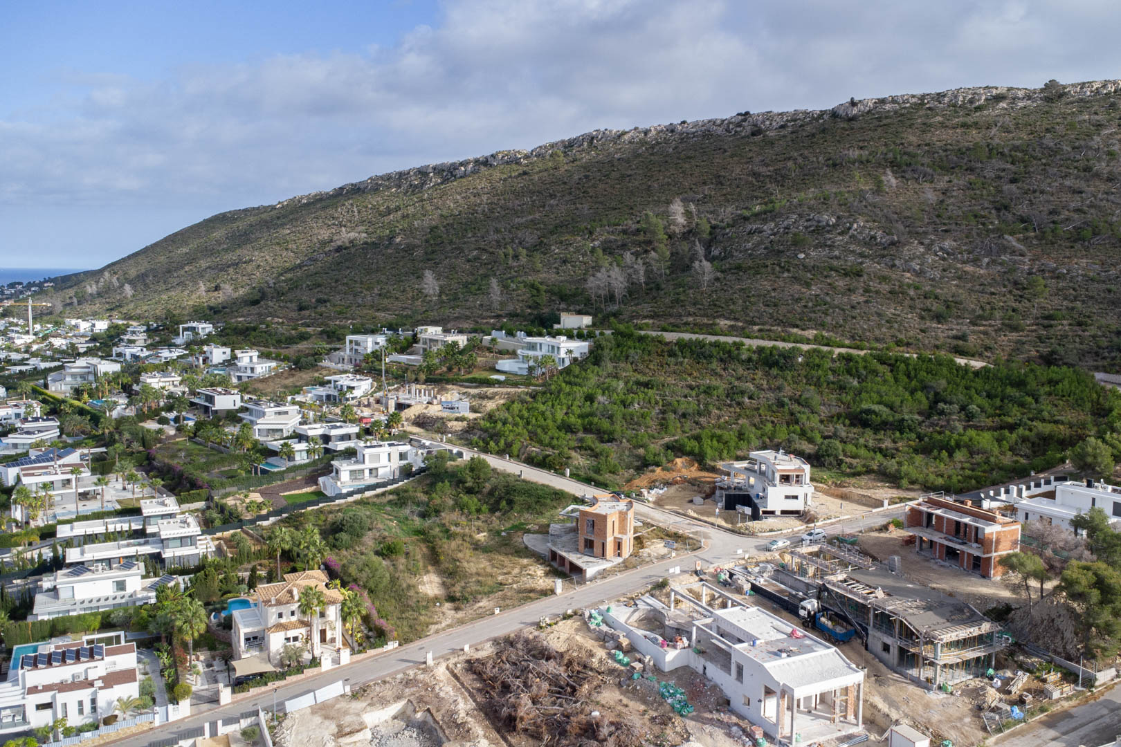 Aerial view of the Monte Olímpico residential area, featuring fully urbanized plots with paved roads, street lighting, and contemporary villas near the hillside.