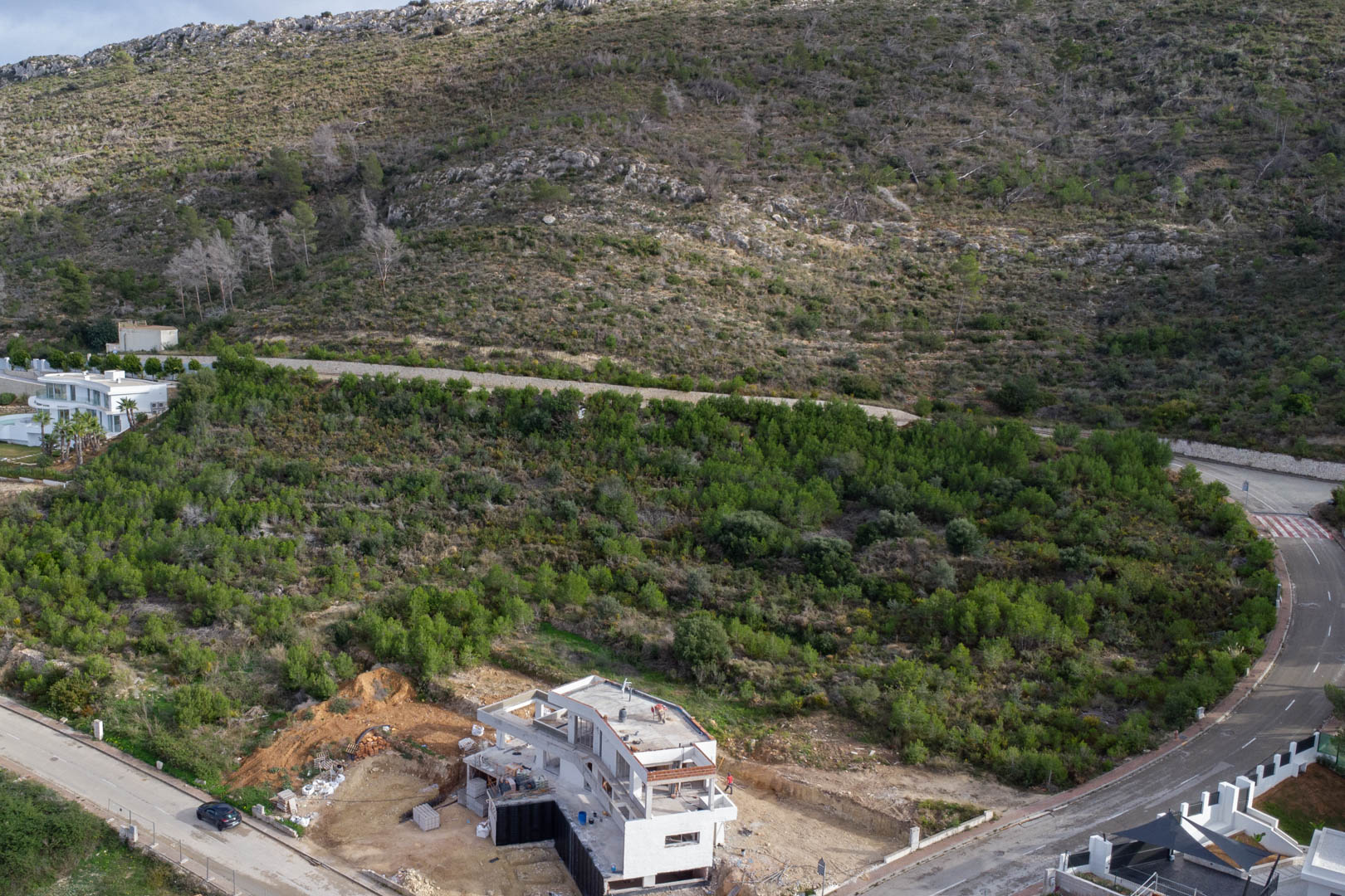 Aerial view of the plot in Monte Olímpico, featuring completed urban infrastructure and a villa under construction amidst Mediterranean greenery.