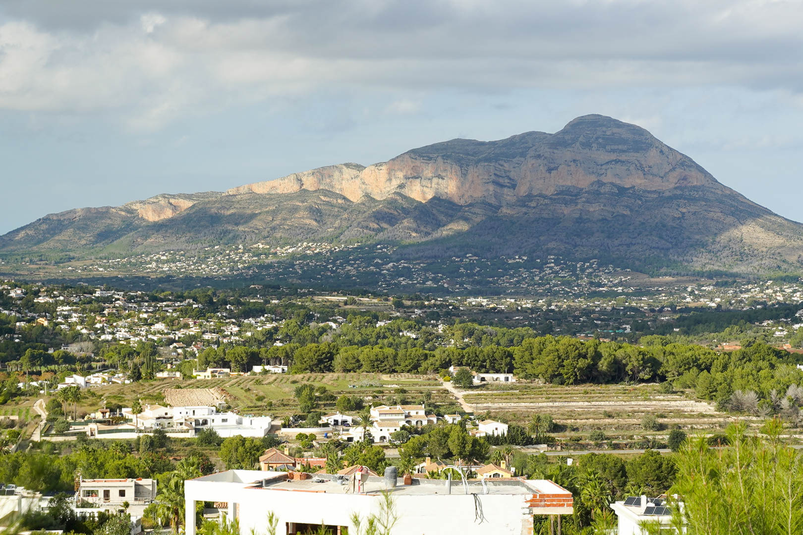 Panoramic view of the Montgó mountain range from the plot, overlooking white Mediterranean villas and lush pine groves under soft natural daylight.