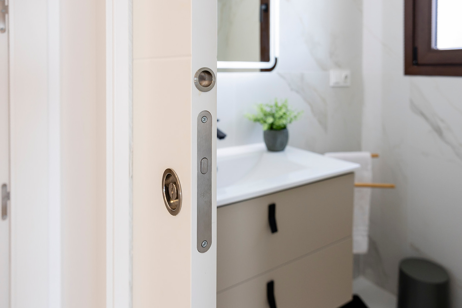 Close-up of a white sliding door with metallic hardware, opening into a modern bathroom featuring marble-effect tiling and a contemporary vanity unit.