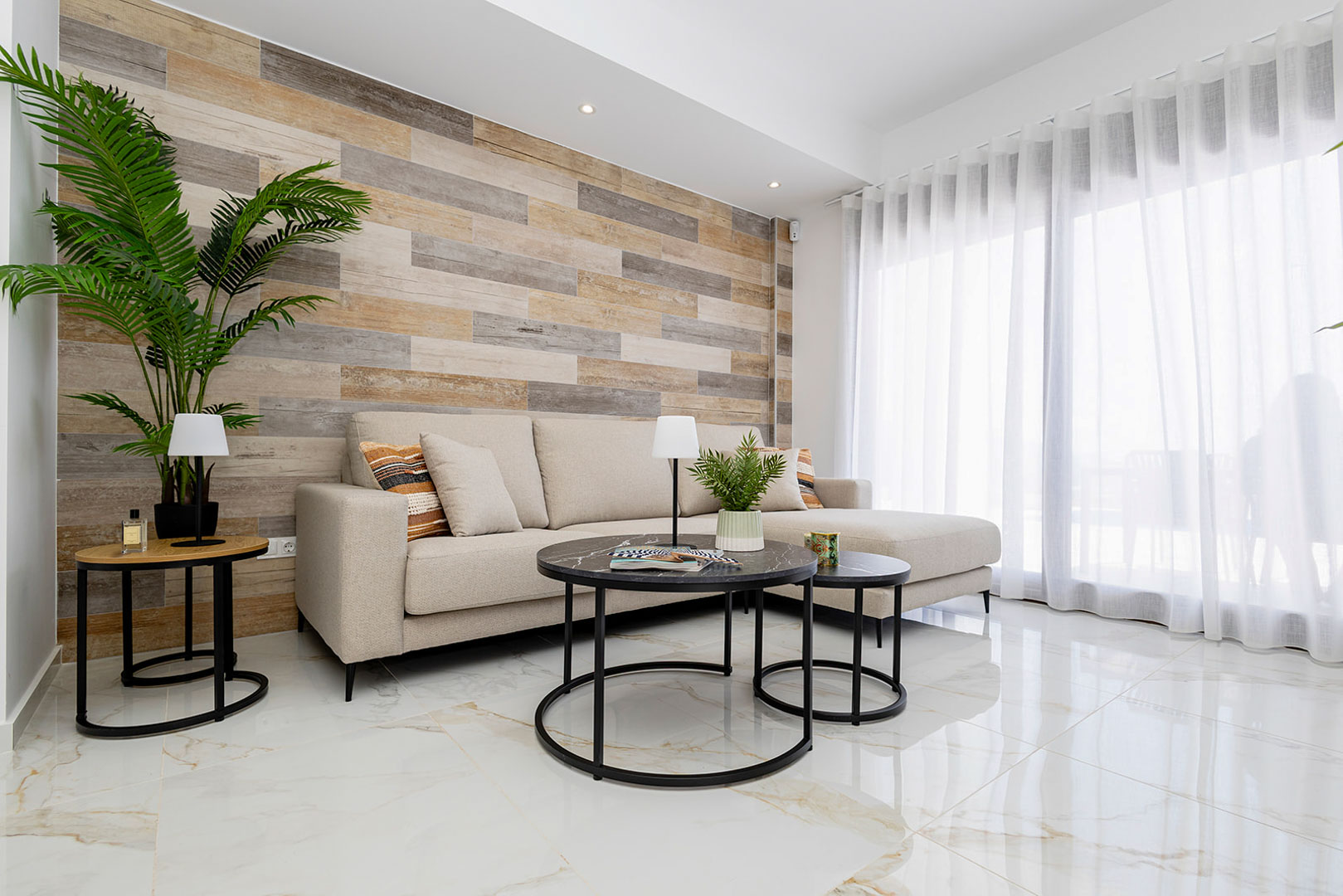 Living area featuring a wood-plank accent wall, polished marble-effect flooring, and a beige sectional sofa illuminated by natural light from large sliding doors.