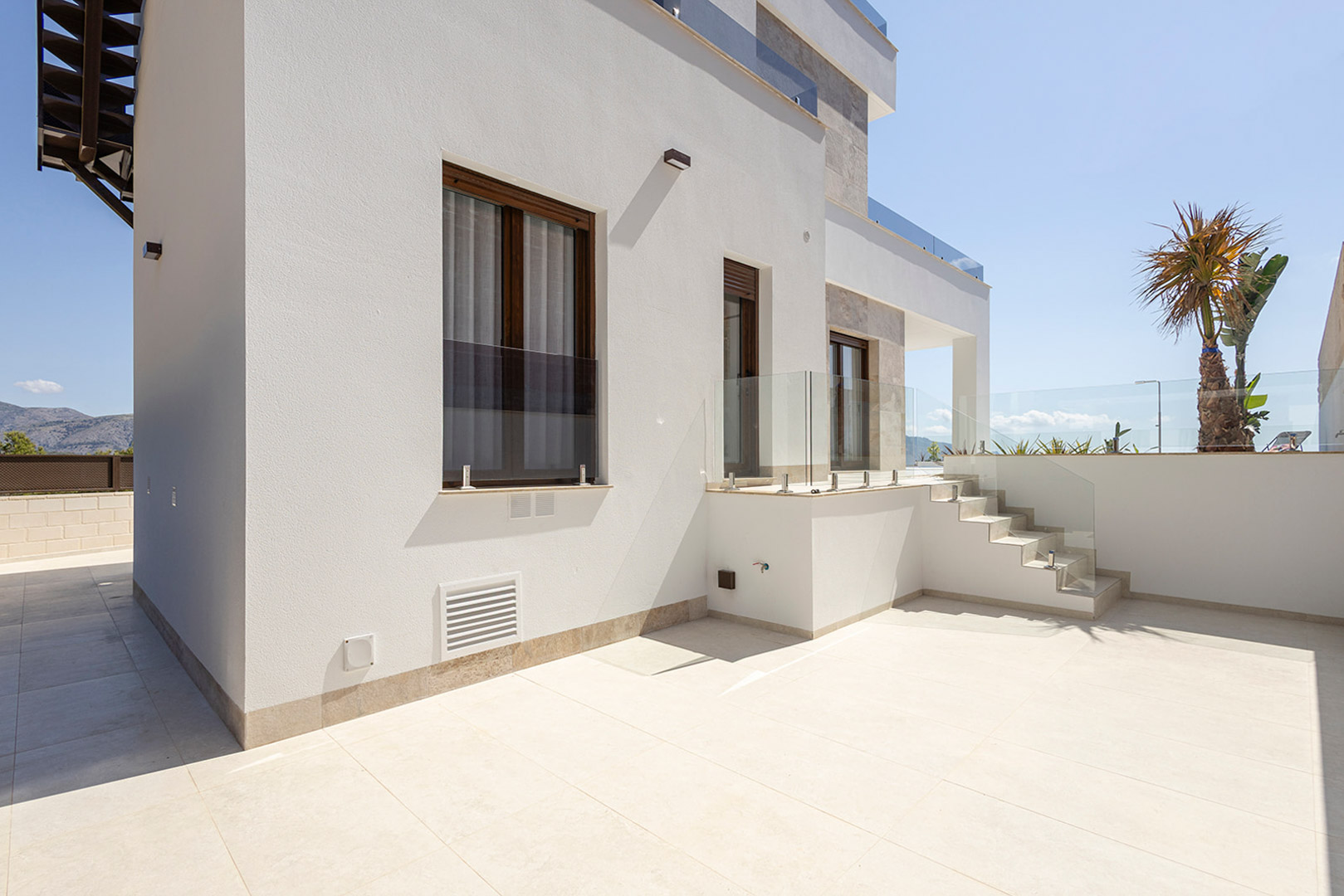 Minimalist exterior featuring white facades, dark window frames, and spacious tiled terraces with sleek glass balustrades.