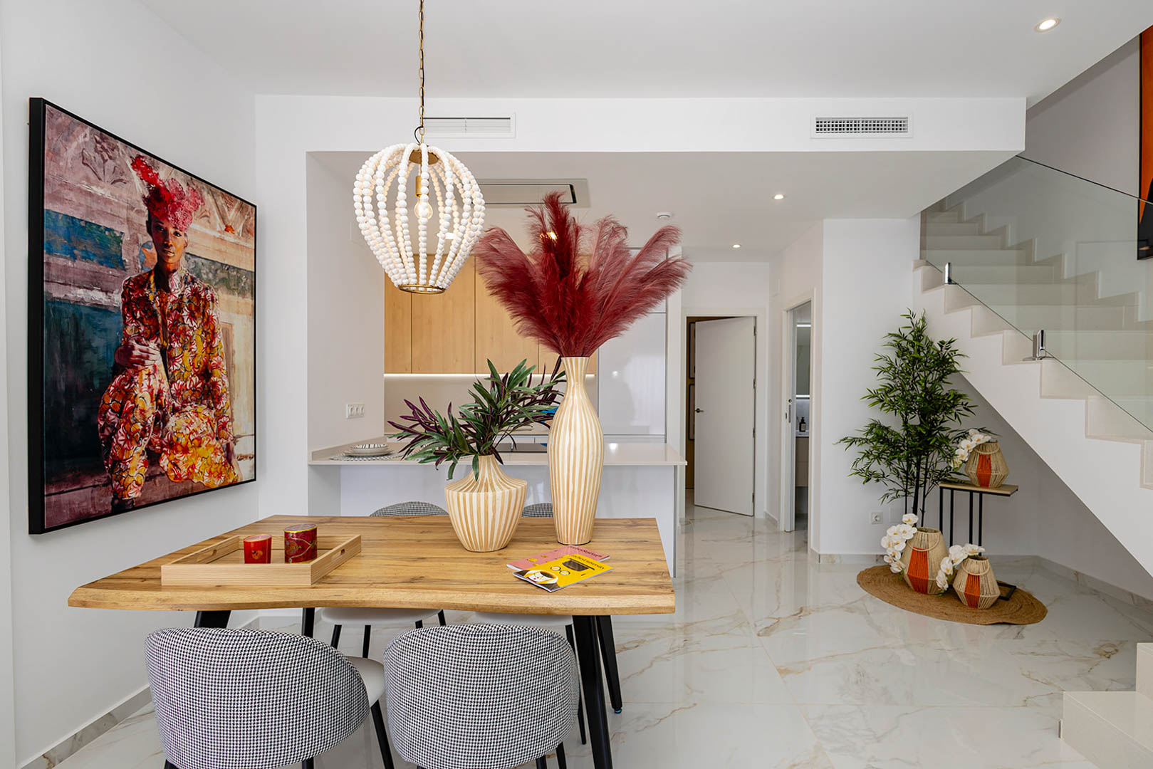 Open-concept dining area featuring a natural wood table, beaded pendant light, and marble-effect porcelain flooring adjacent to a modern staircase with glass railings.