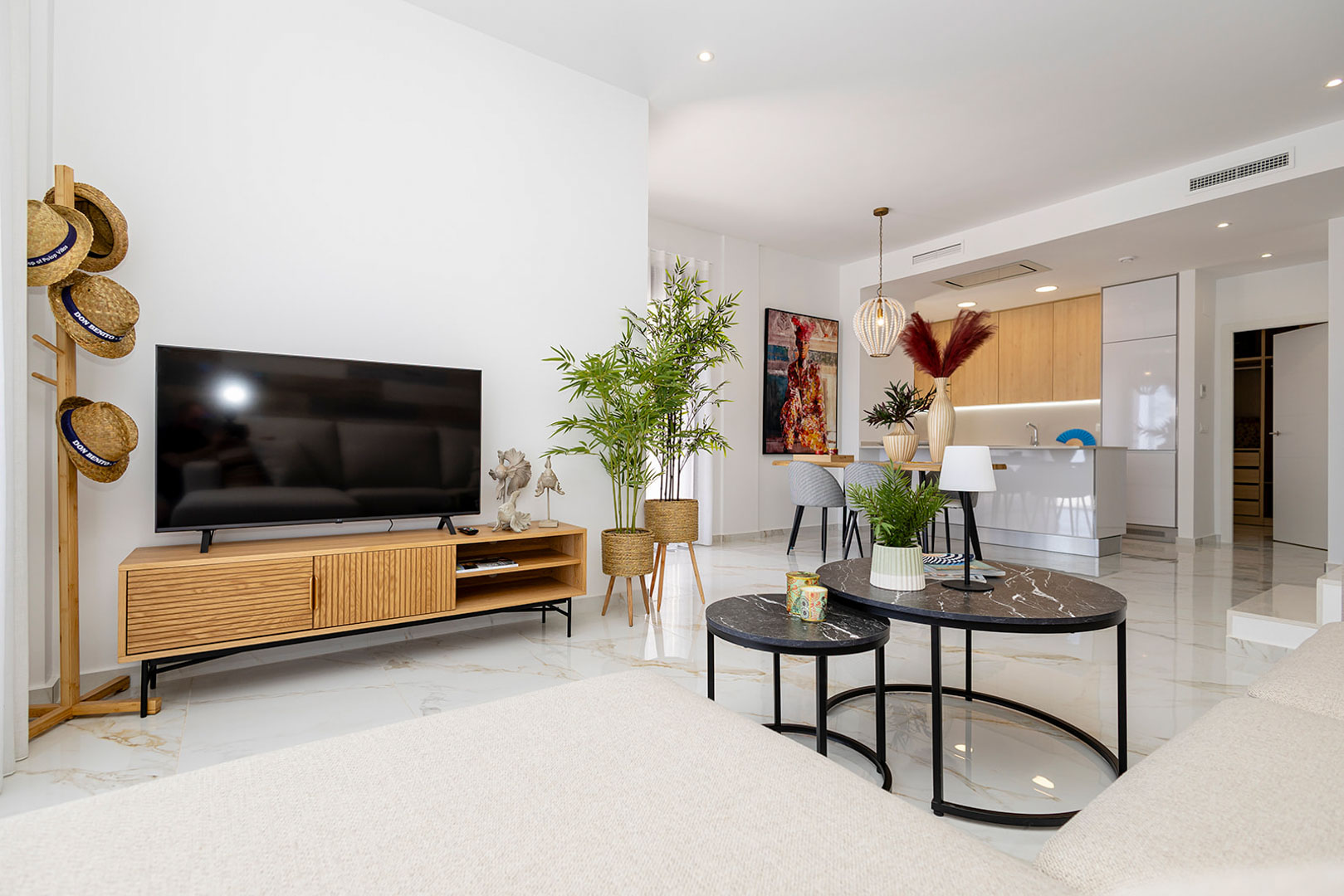 Open-concept living room featuring marble-effect porcelain flooring, natural wood media console, and a modern kitchen with a white island and integrated cabinetry.