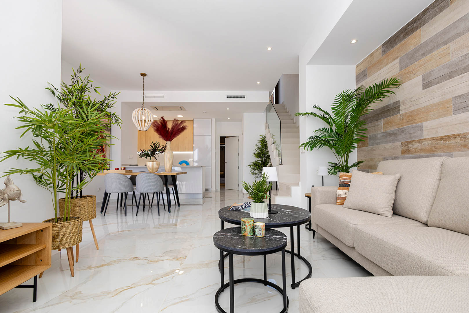 Open-plan living area featuring marble-effect porcelain flooring, a wood-textured accent wall, and a modern staircase with glass balustrade.