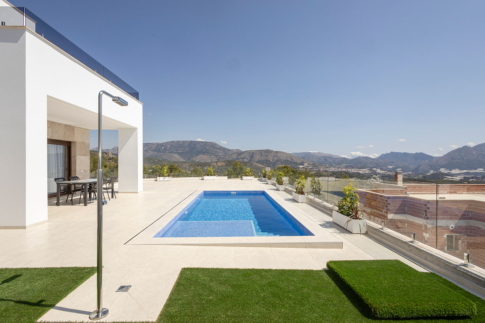 Outdoor terrace featuring a private pool, stainless steel shower, and covered dining area, with glass railings overlooking the mountain landscape.