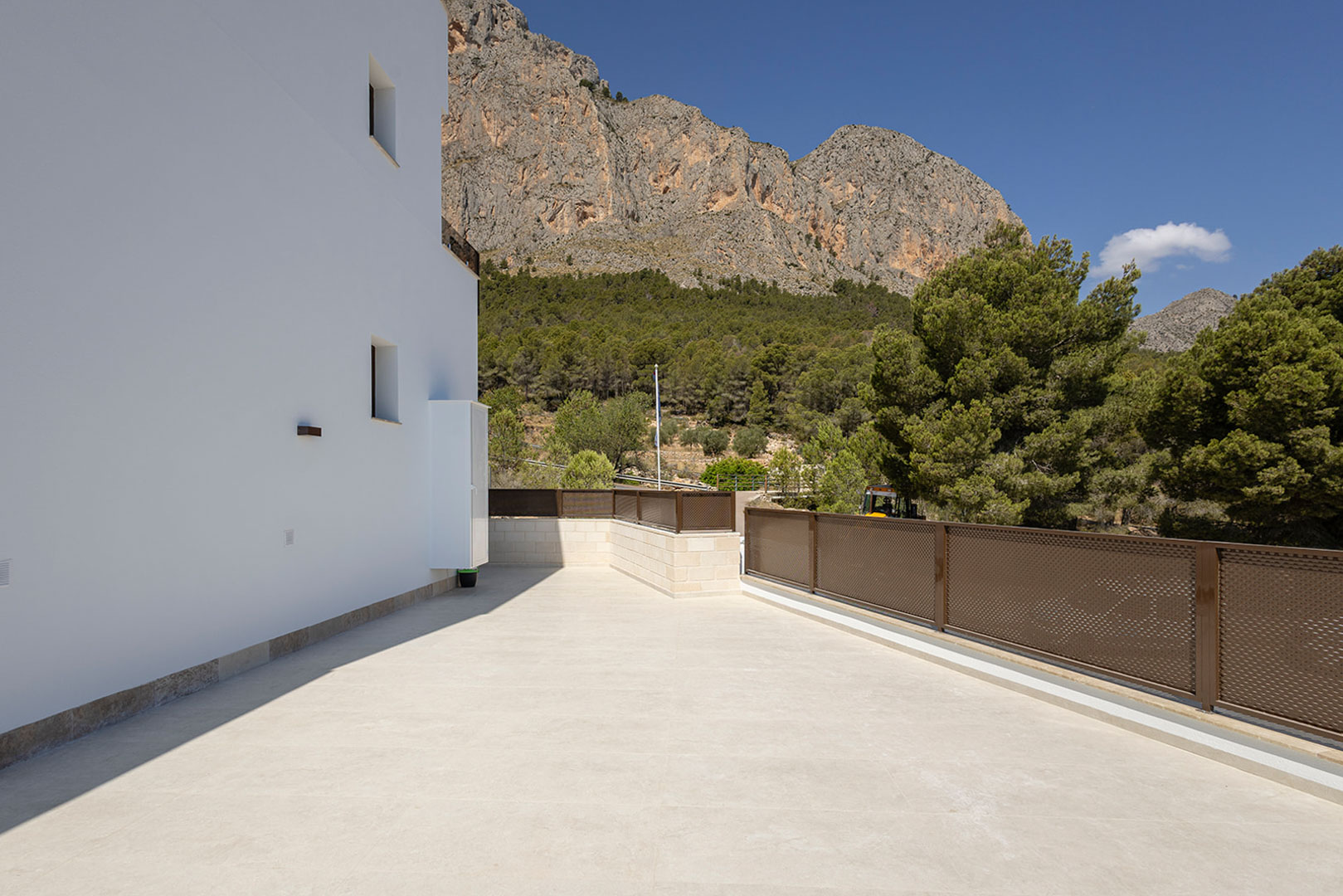 Outdoor terrace featuring light stone tiling and perforated metal railings, providing panoramic views of the rugged mountain landscape and pine forest.