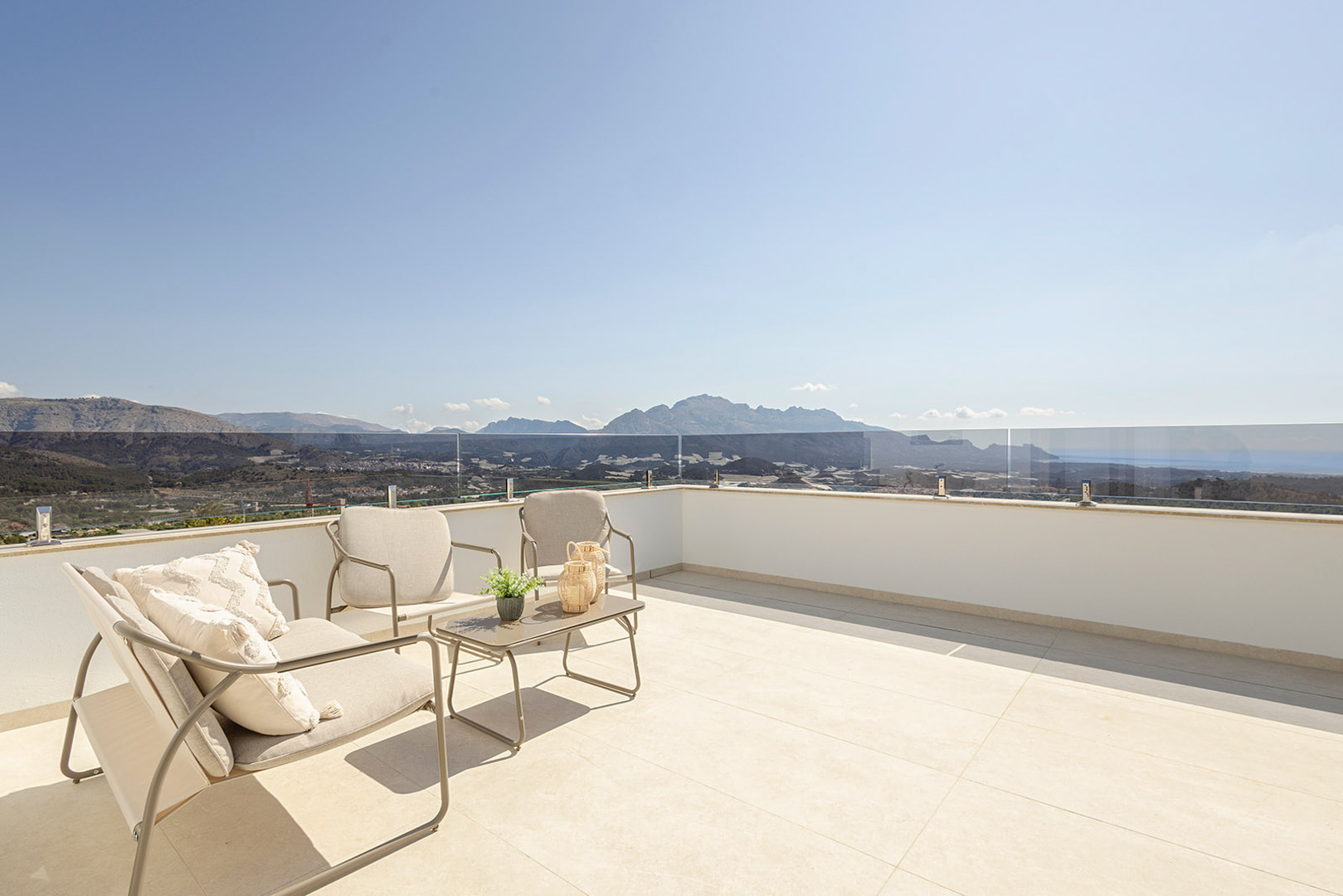 Rooftop terrace featuring light-toned tiling, glass balustrades, and minimalist outdoor furniture with panoramic sea and mountain views.