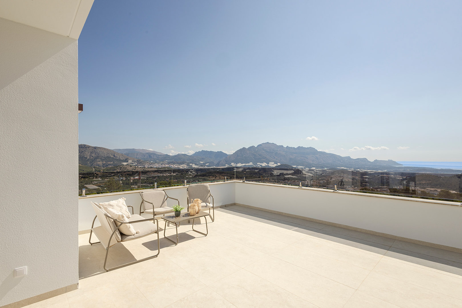 Upper terrace featuring a glass balustrade, modern outdoor lounge furniture, and panoramic mountain and sea views. Finished with large-format light floor tiles.