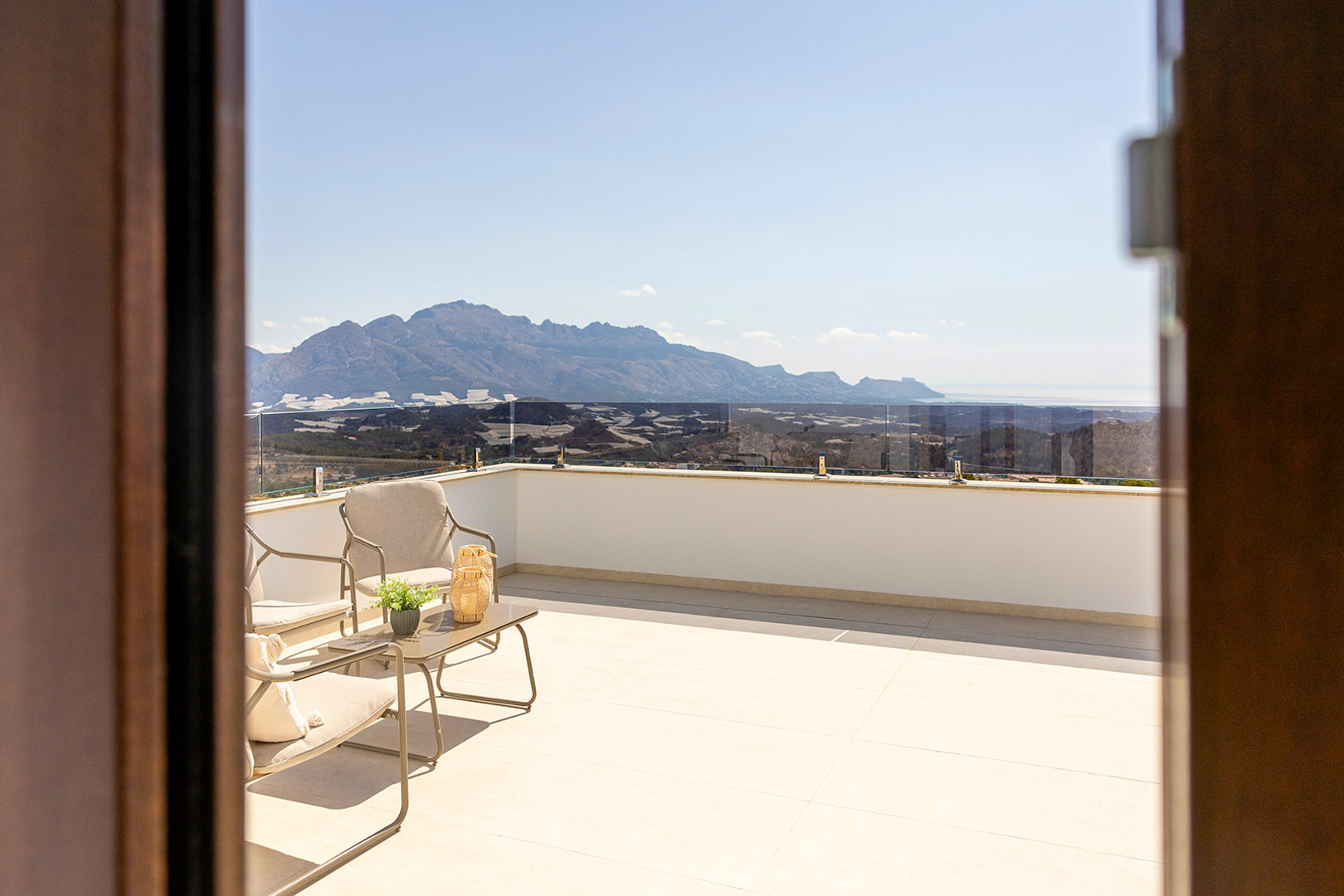 Upper terrace with glass balustrades, modern outdoor furniture, and unobstructed panoramic views of the mountains and the Mediterranean Sea.