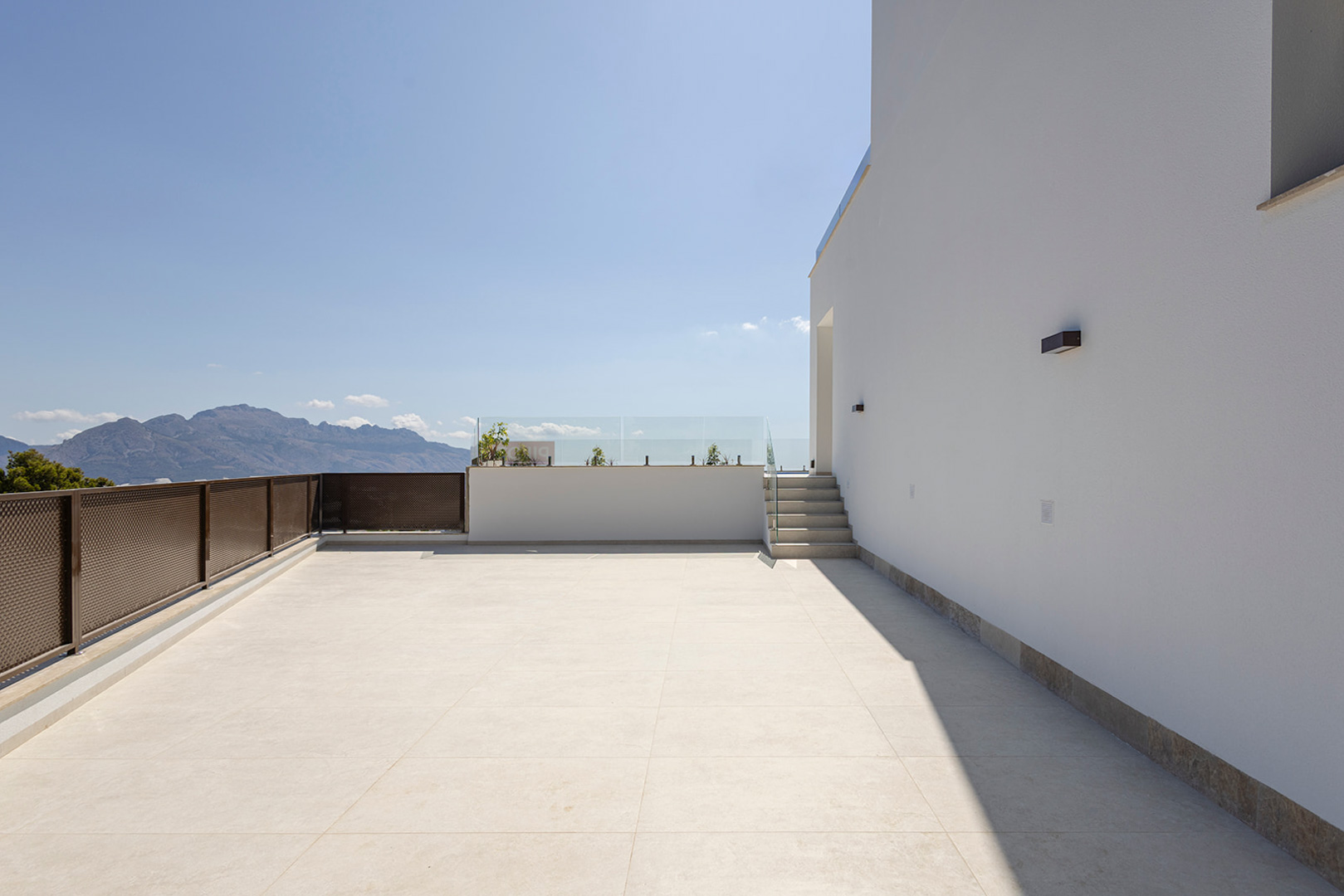 Upper terrace with light ceramic flooring, glass balustrades, and unobstructed mountain views. Features modern outdoor lighting on the minimalist white facade.