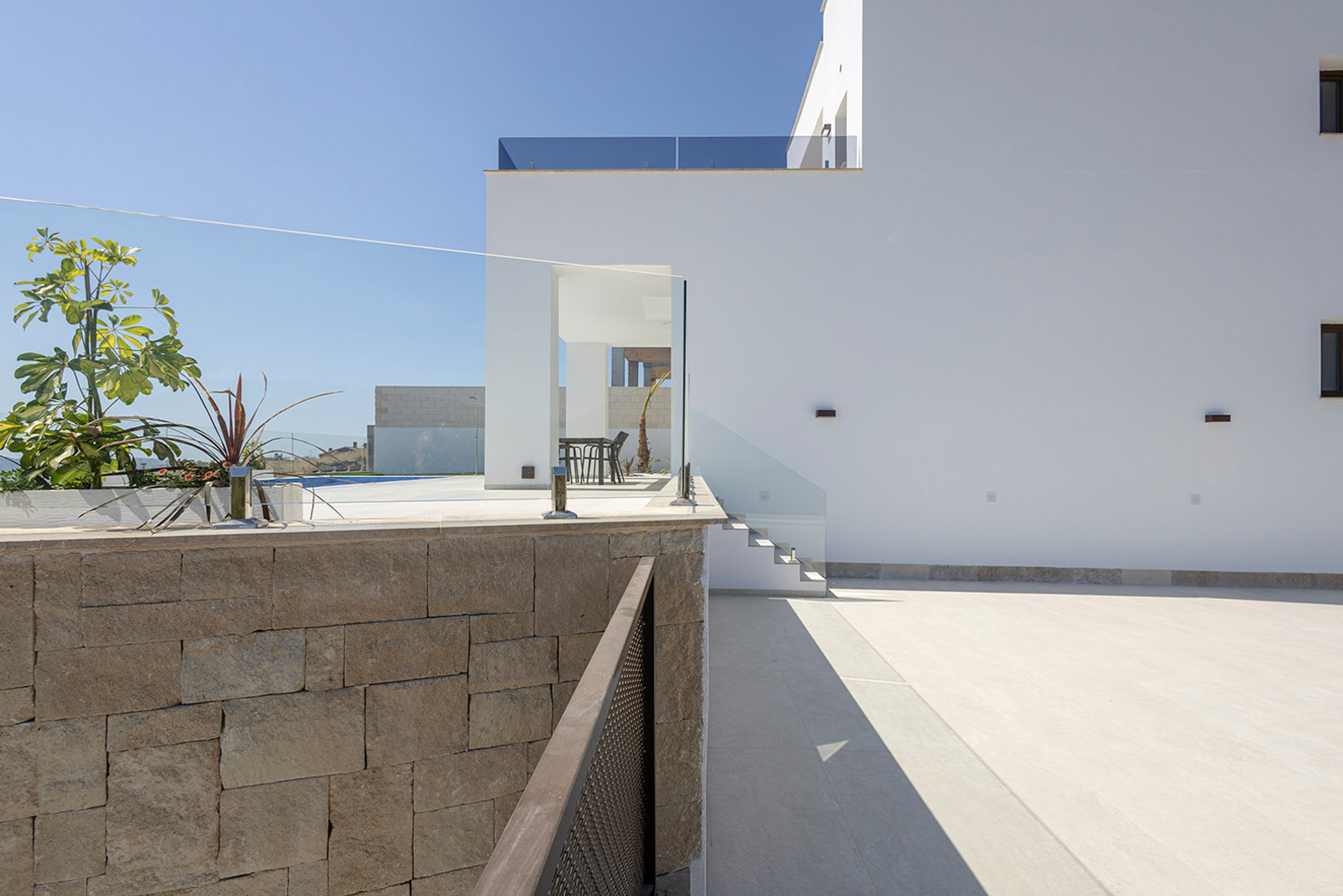 White modern facade featuring a natural stone retaining wall, glass balustrades, and a paved outdoor area leading to the upper terrace level.