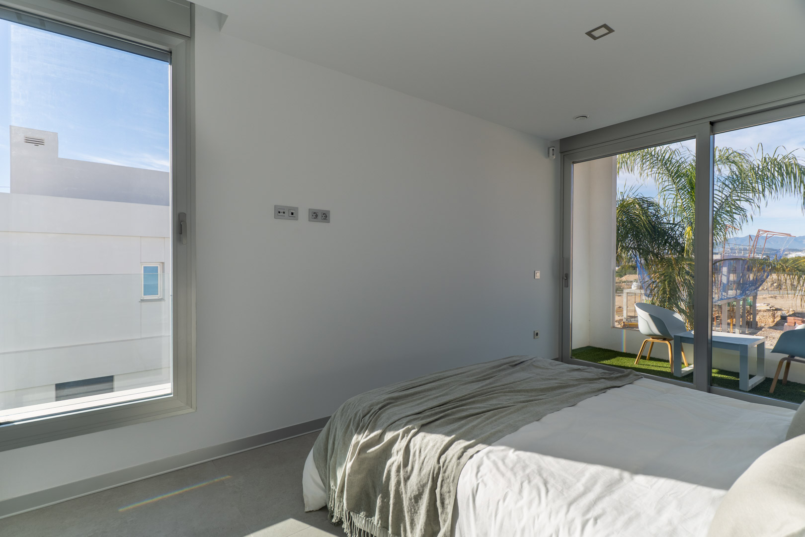 Bright bedroom featuring direct access to a private balcony with artificial turf. The space offers minimalist decor, grey tiled flooring, and abundant natural light.