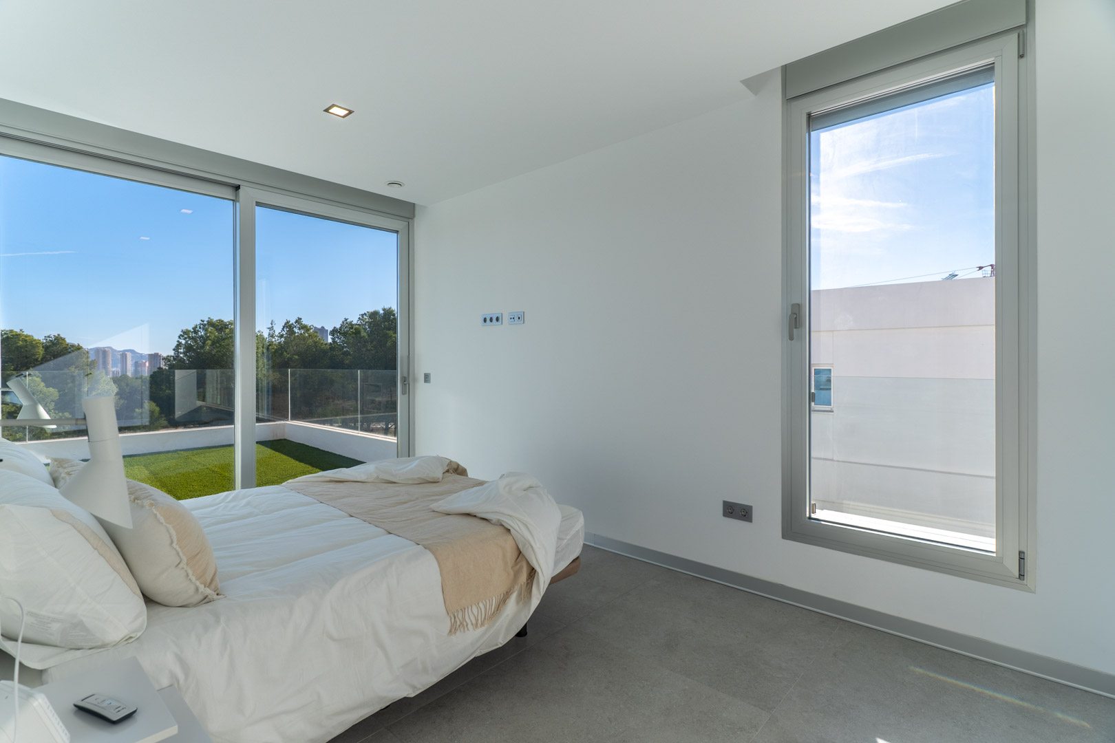 Bright bedroom featuring grey tiled floors, large sliding glass doors, and direct access to a private terrace with artificial turf and panoramic views.