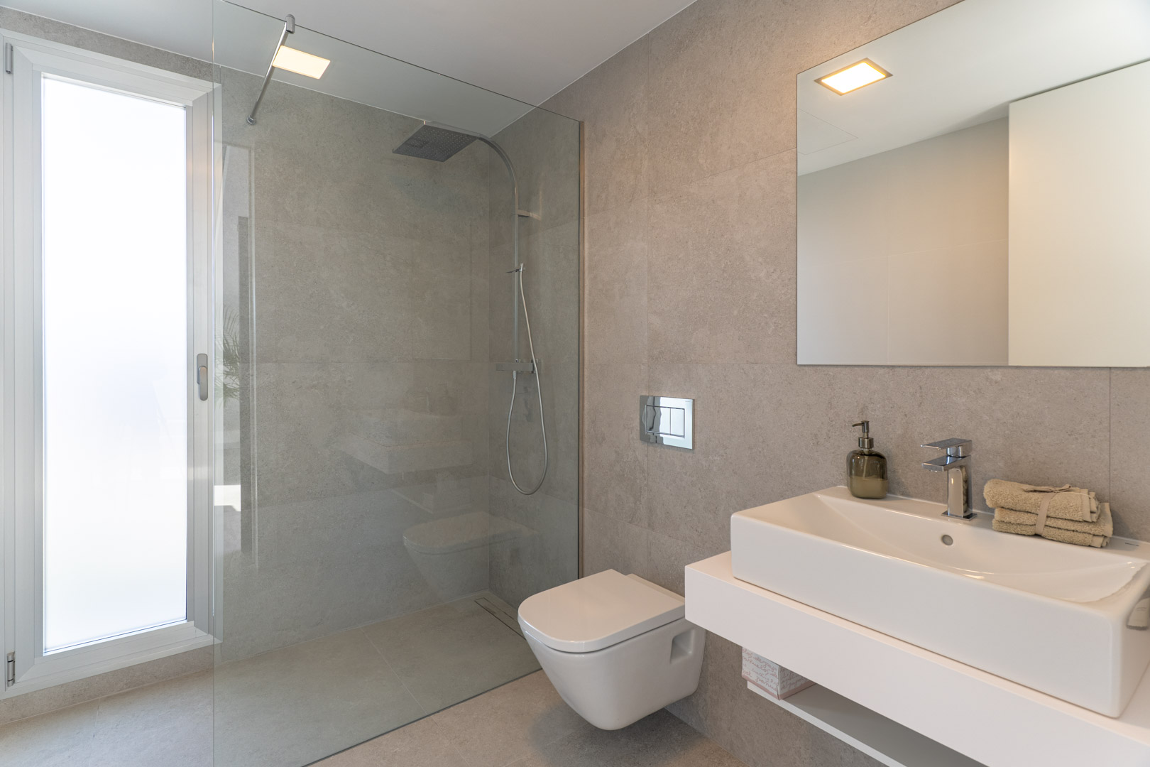 Modern bathroom featuring grey stone-effect tiling, a walk-in glass shower, wall-hung toilet, and a minimalist floating vanity with a rectangular sink.