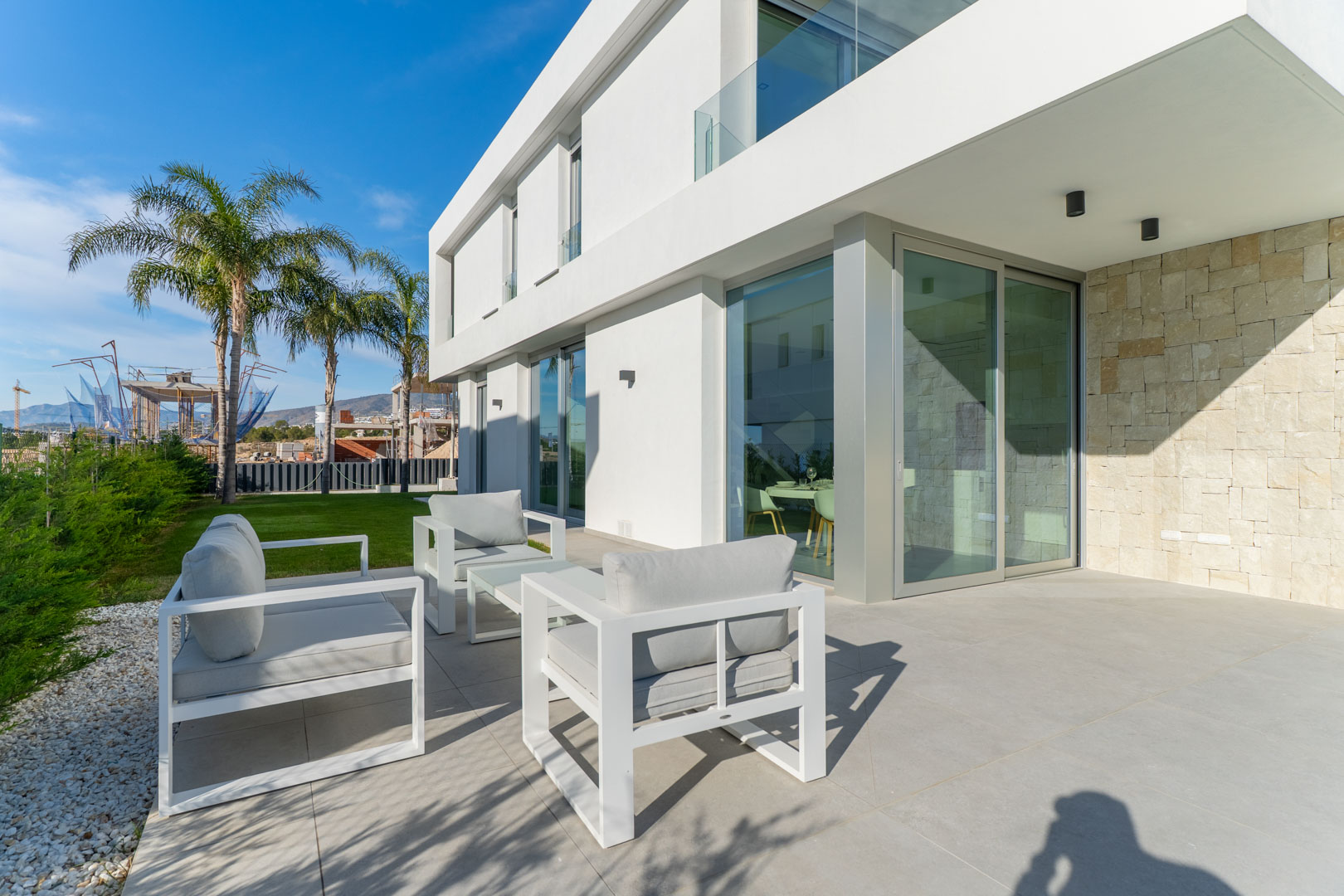 Outdoor terrace featuring minimalist white seating, porcelain tile flooring, and a facade blending white finishes with a textured natural stone wall.