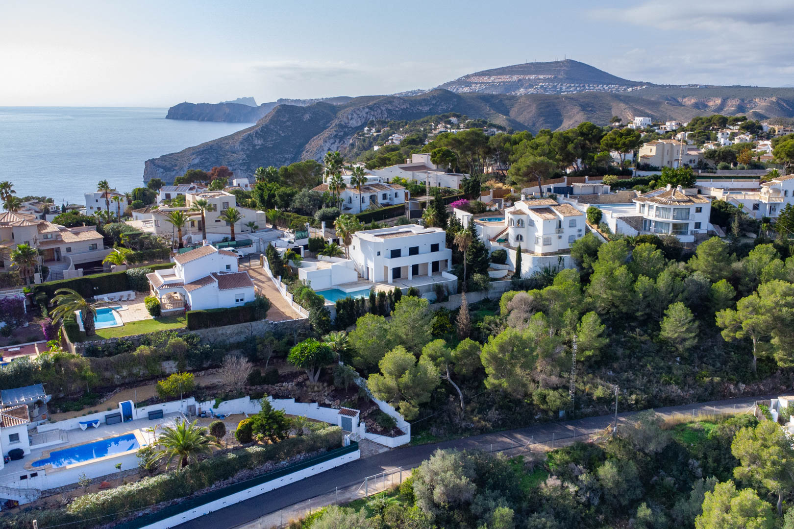 Aerial perspective of the Granadella-Ambolo residential area, featuring hillside villas surrounded by pine forests with views of the Mediterranean Sea.