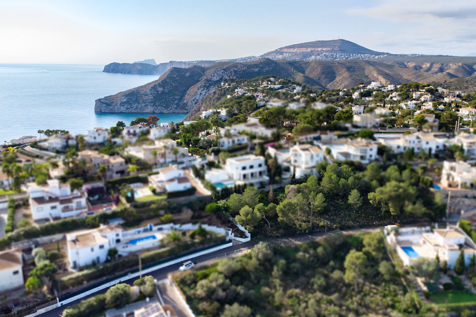 Aerial tilt-shift view of the Granadella-Ambolo residential area, featuring white villas nestled among pine trees along the Mediterranean coast.