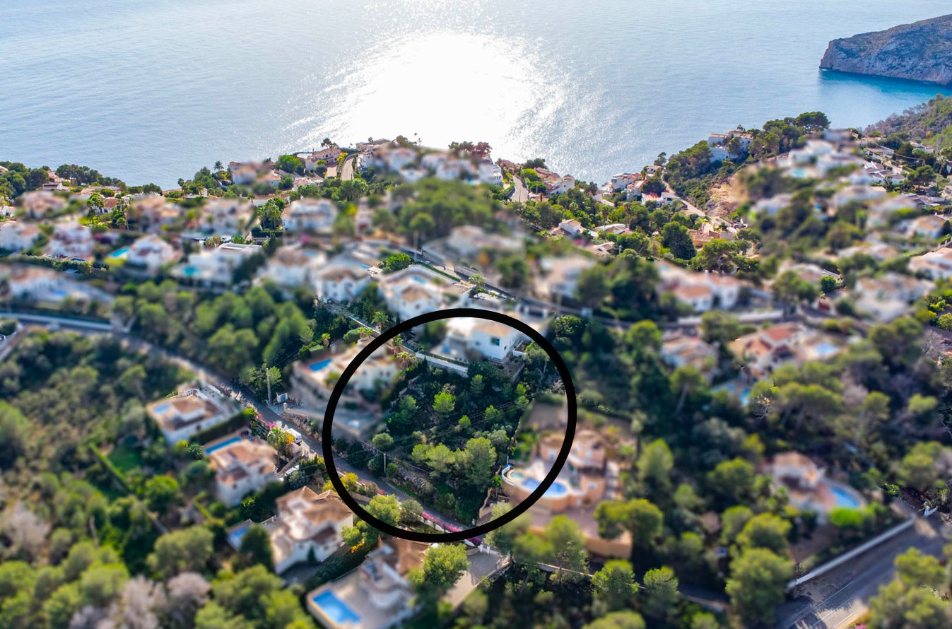 Aerial view of the 1042m2 building plot featuring sloped terrain and Mediterranean pines, situated in an established residential area with coastal views.