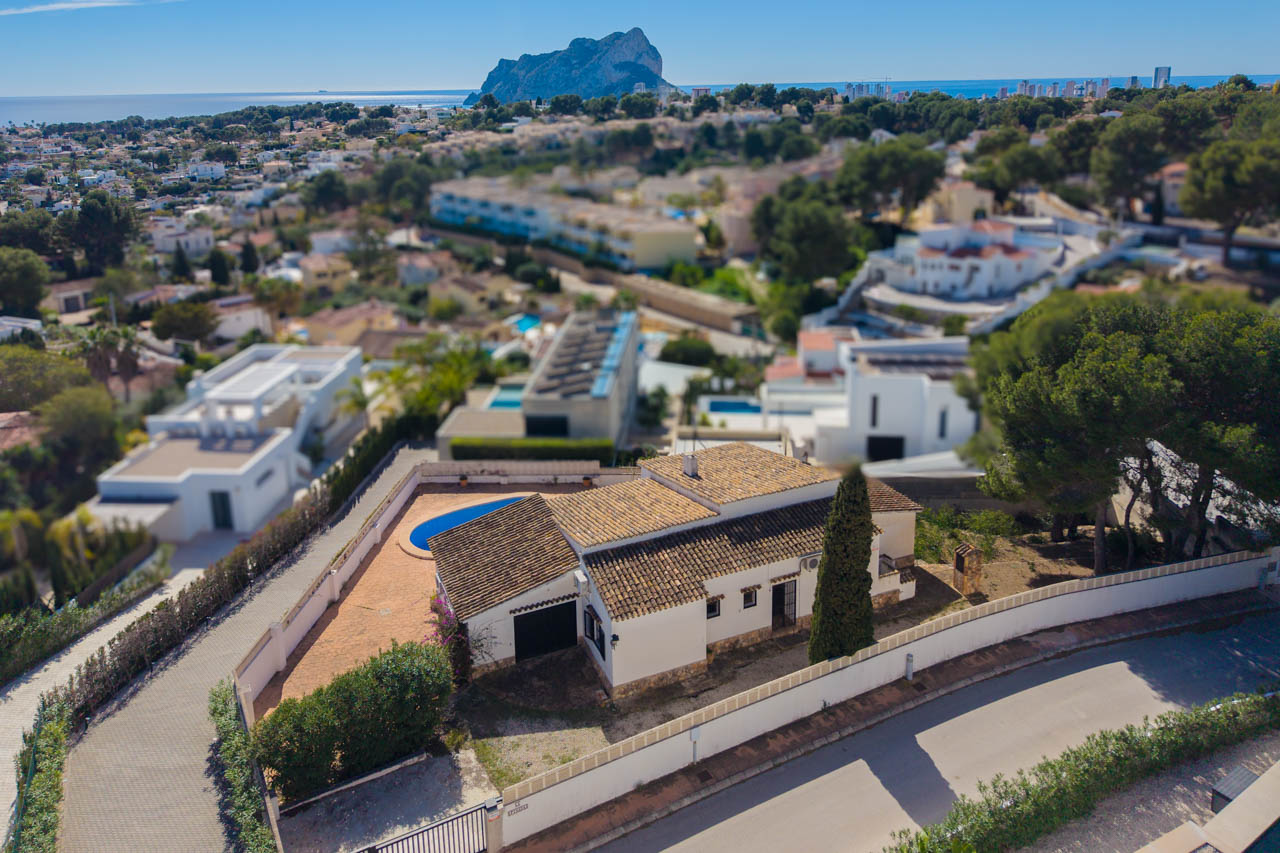 Aerial perspective of the Mediterranean villa featuring a tiled roof, private pool, and expansive views of the sea and the Peñón de Ifach rock formation.
