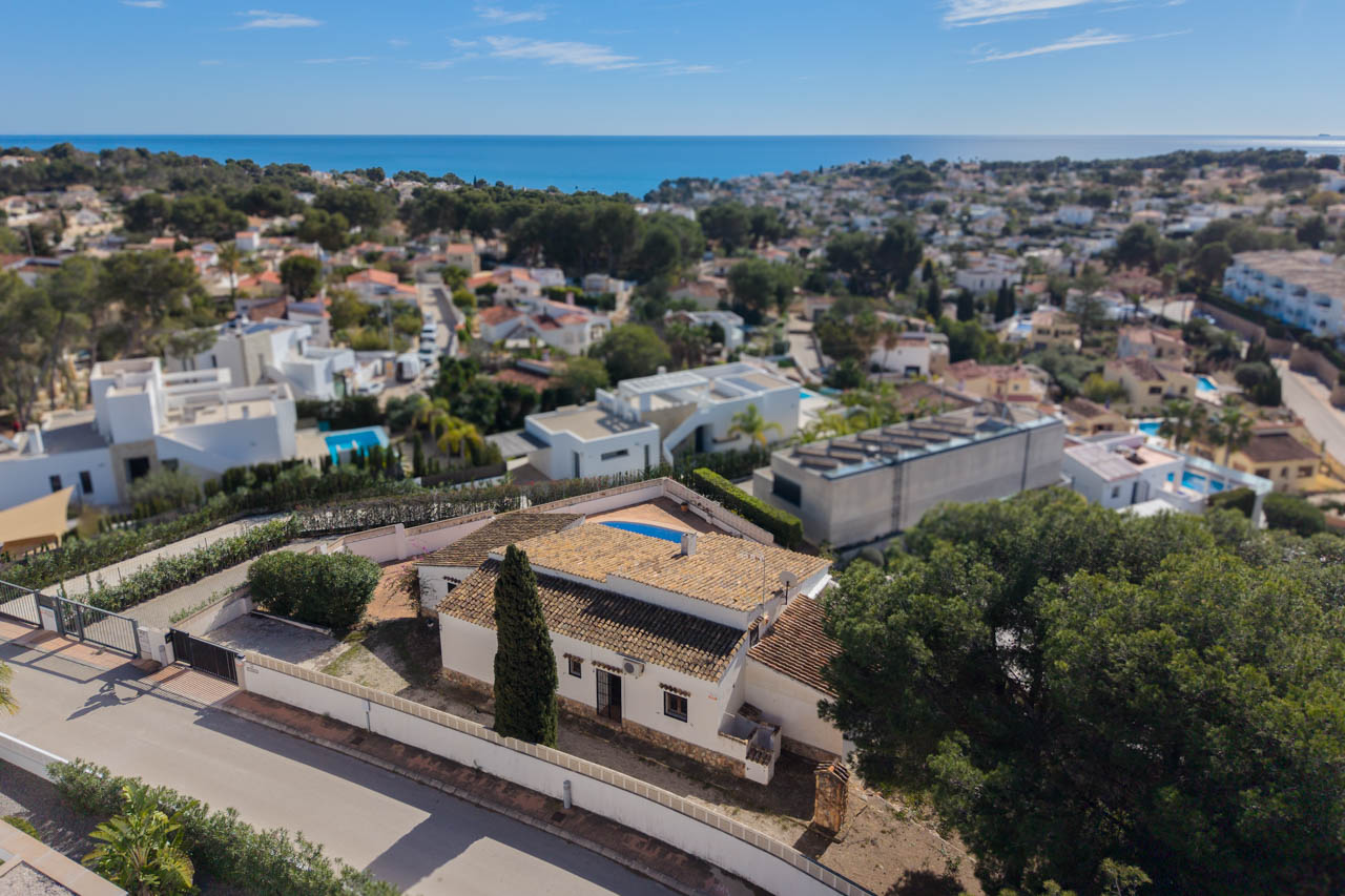 Aerial perspective of the villa in Benissa Costa, showcasing the traditional tiled roof, private plot with cypress trees, and panoramic Mediterranean Sea views.
