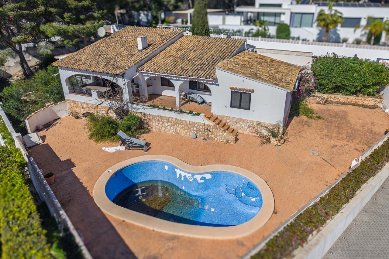 Aerial view of the Mediterranean villa featuring an organic-shaped pool, expansive paved terraces, and arched porches. The exterior includes natural stone walls and clay tile roofing.