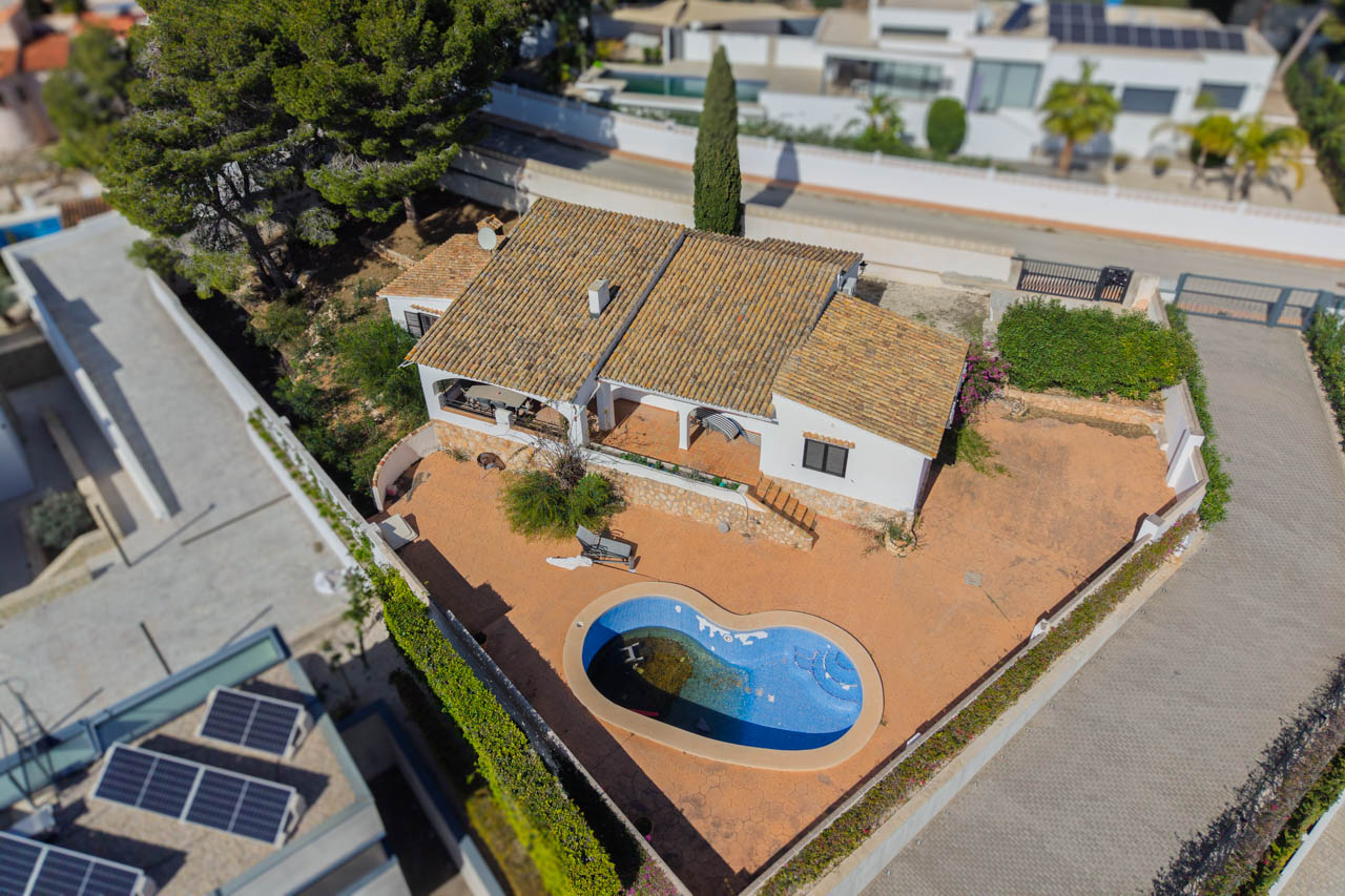 Aerial view of the villa featuring a flat plot, an organic-shaped swimming pool, and traditional Mediterranean architecture with terracotta roof tiles.