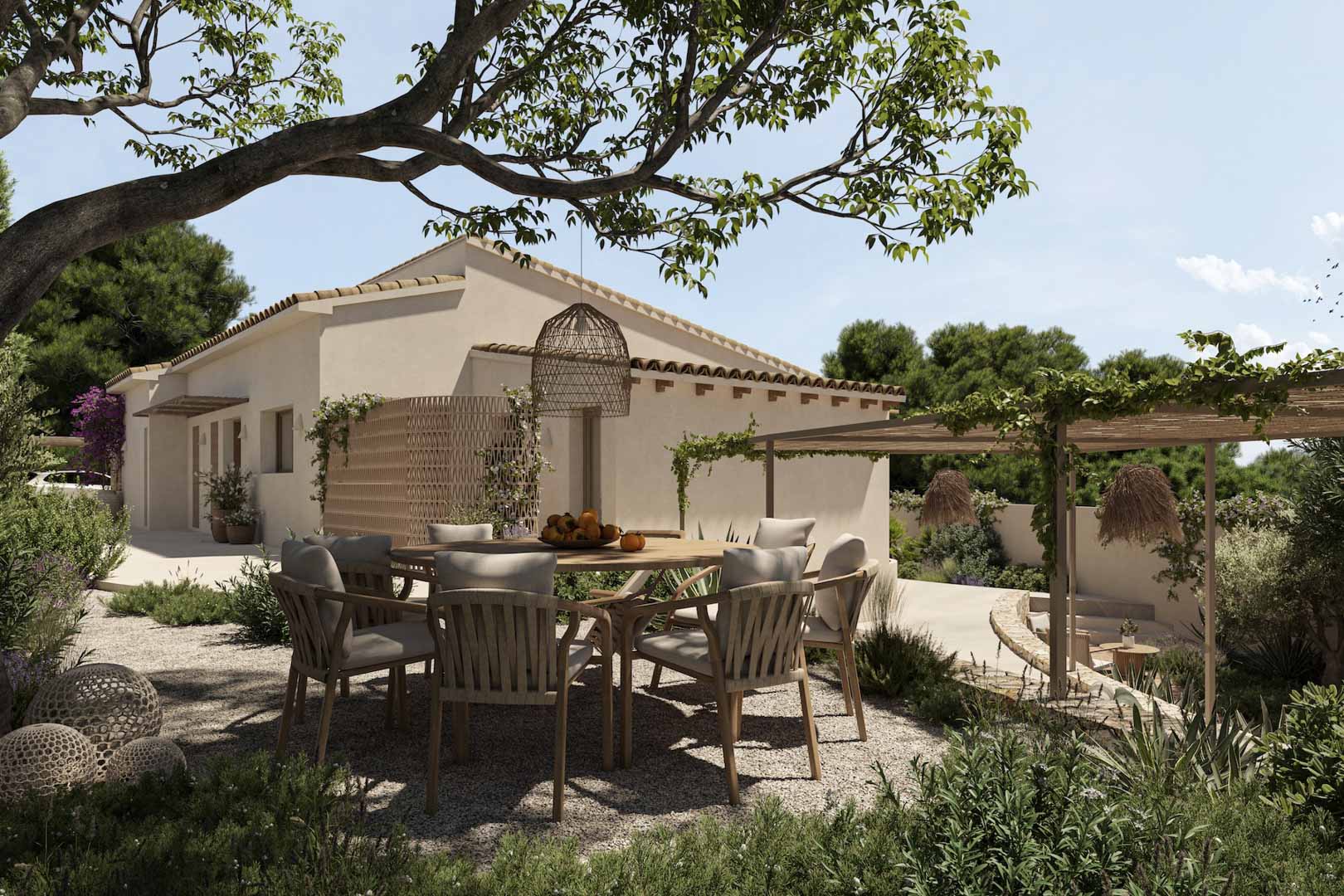 Outdoor dining area with a round wooden table and woven chairs on a gravel terrace, shaded by mature trees and a pergola with climbing vines.