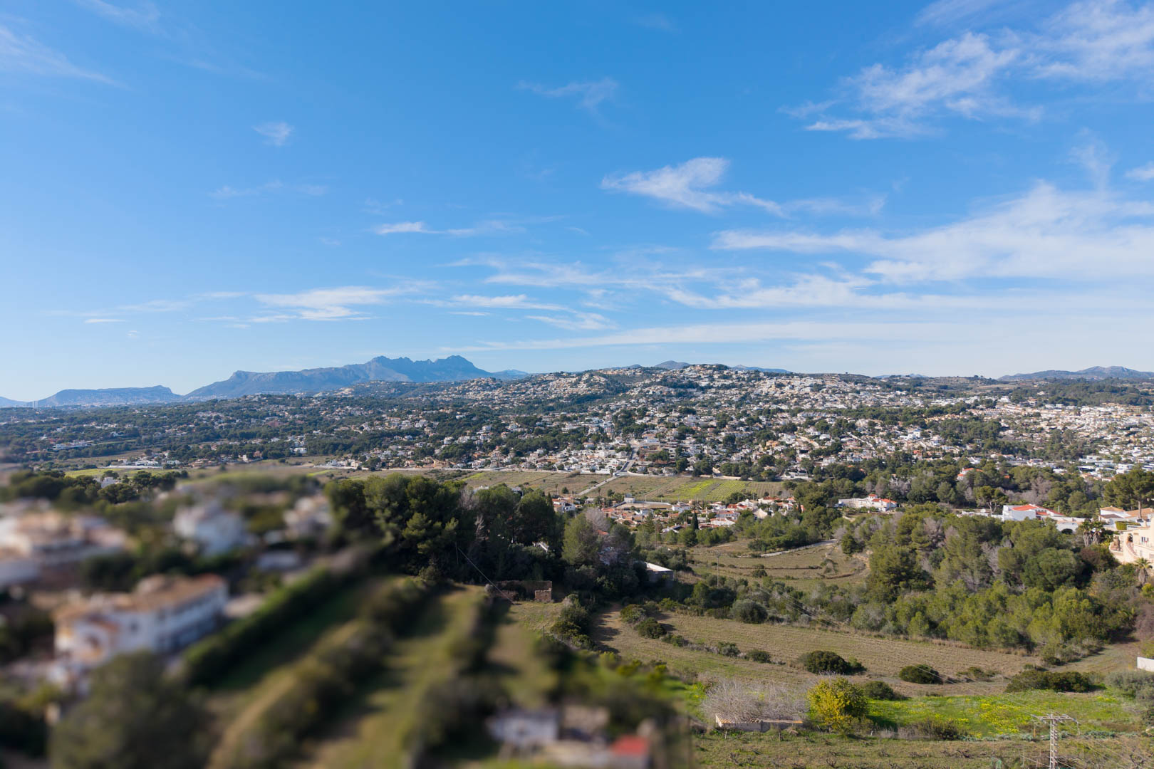 Elevated panoramic view of the Moraira valley, featuring residential areas integrated into the Mediterranean landscape with distant mountain silhouettes.