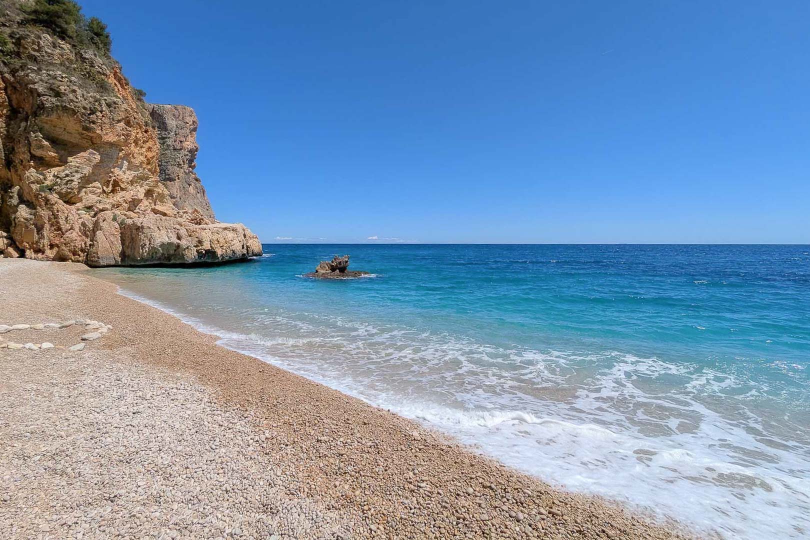 View of a pebble beach with turquoise Mediterranean waters and limestone cliffs, located near the exclusive coastal town of Moraira.