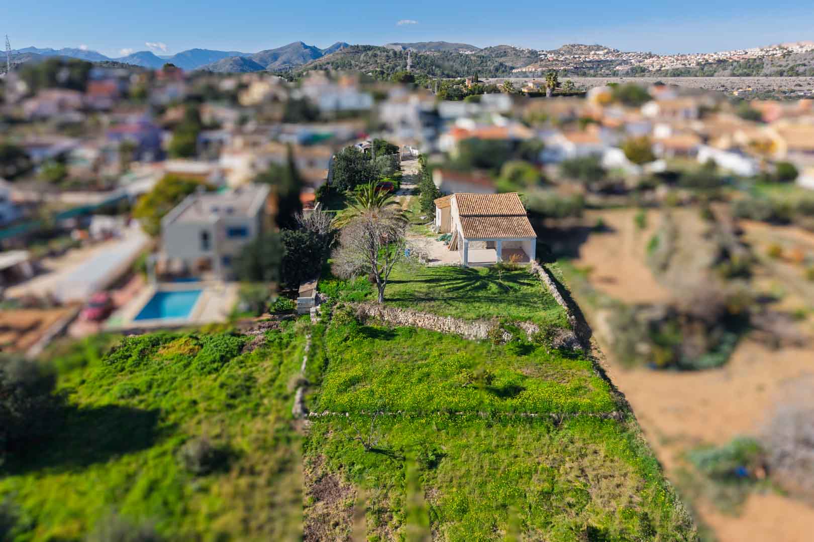 Aerial perspective of the finca featuring a renovated tiled roof and naya, set on an elongated plot with dry stone walls and views of the surrounding mountains.
