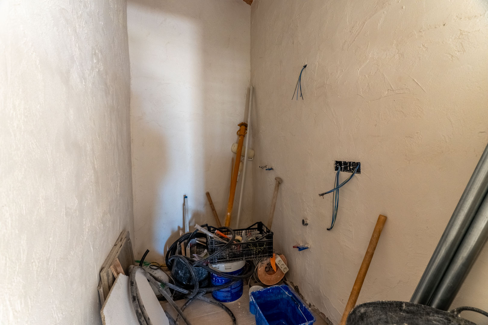Interior room under renovation featuring plastered walls, exposed electrical wiring, and various construction materials indicating ongoing infrastructure work.
