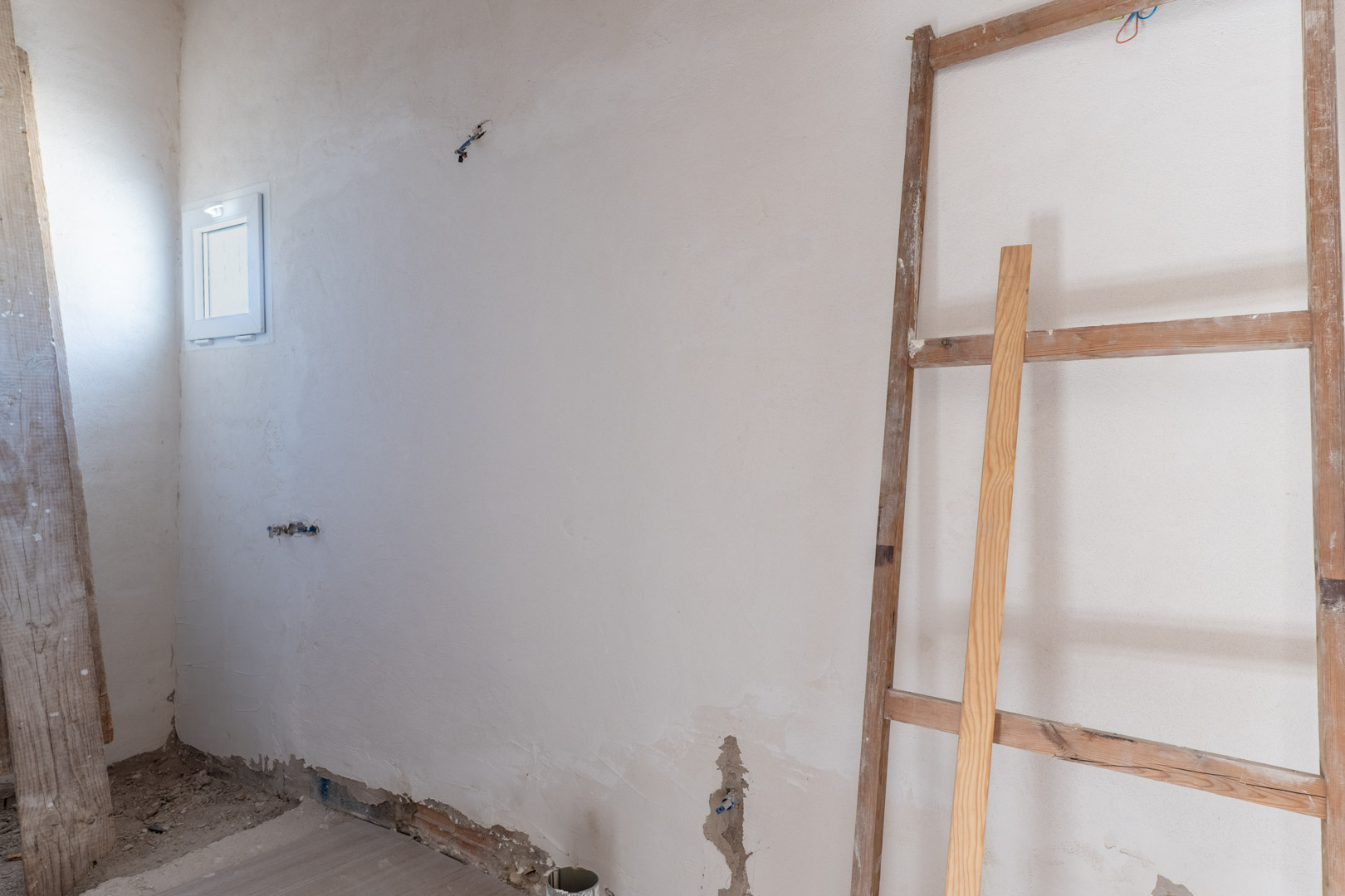 Interior room undergoing renovation with freshly plastered walls, a small white-framed window, and electrical wiring ready for installation.