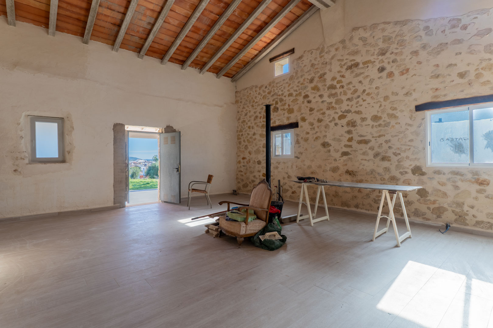 Main living area featuring original dry stone walls, high ceilings with exposed wooden beams and terracotta tiles, providing a bright, open-plan space.