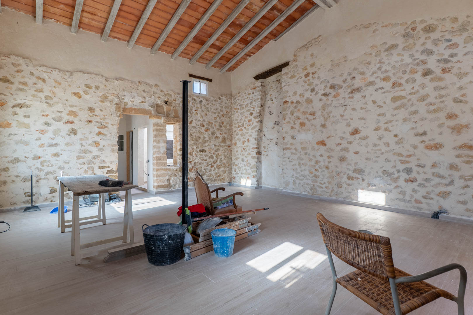 Main room featuring original dry stone walls, high ceilings with exposed wooden beams and clay tiles, and newly laid flooring that preserves the property's rustic character.