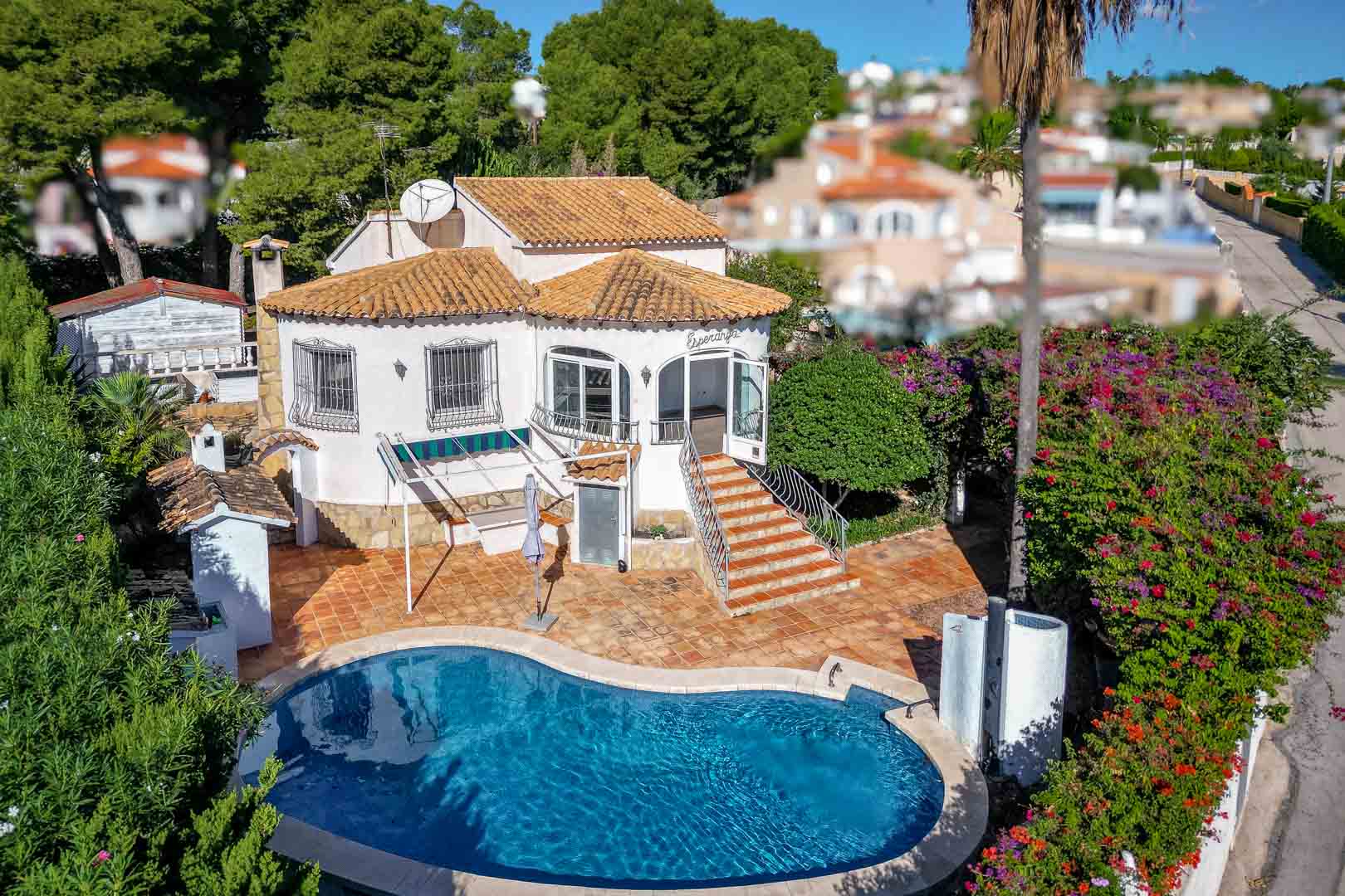 Aerial view of the villa featuring a kidney-shaped pool, terracotta terrace, and main entrance via stairs to a glazed porch, surrounded by Mediterranean gardens.
