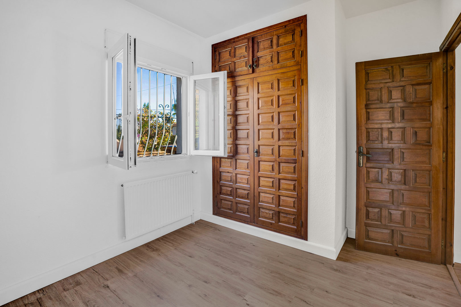 Bedroom featuring a built-in wooden wardrobe with paneled doors, laminate flooring, central heating radiator, and a window providing natural light.