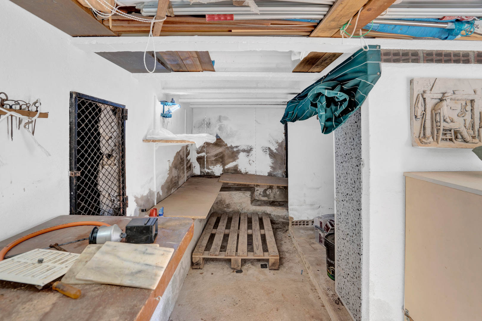 Functional semi-basement storage and workshop area featuring exposed ceiling beams, wooden workbenches, and ample space for tools and maintenance equipment.