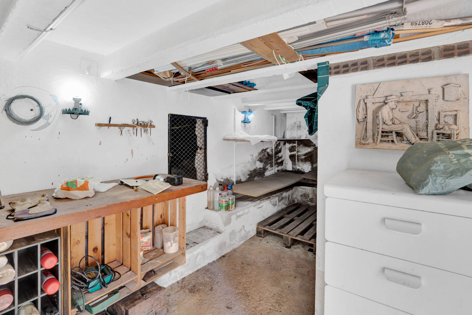 Functional semi-basement storage area featuring a wooden workbench, white-washed walls, and ample space for tools and maintenance equipment.