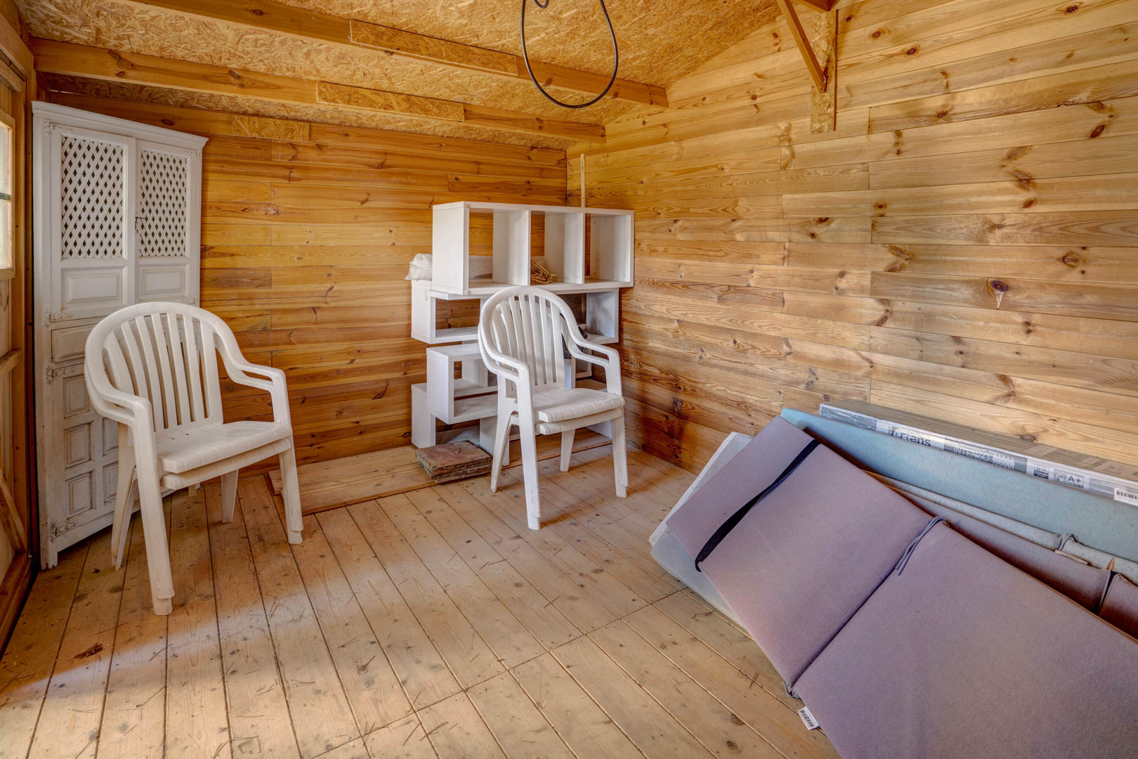 Functional storage room featuring full wood paneling on walls and floors, offering a versatile and dry space for storage or workshop use with natural light.