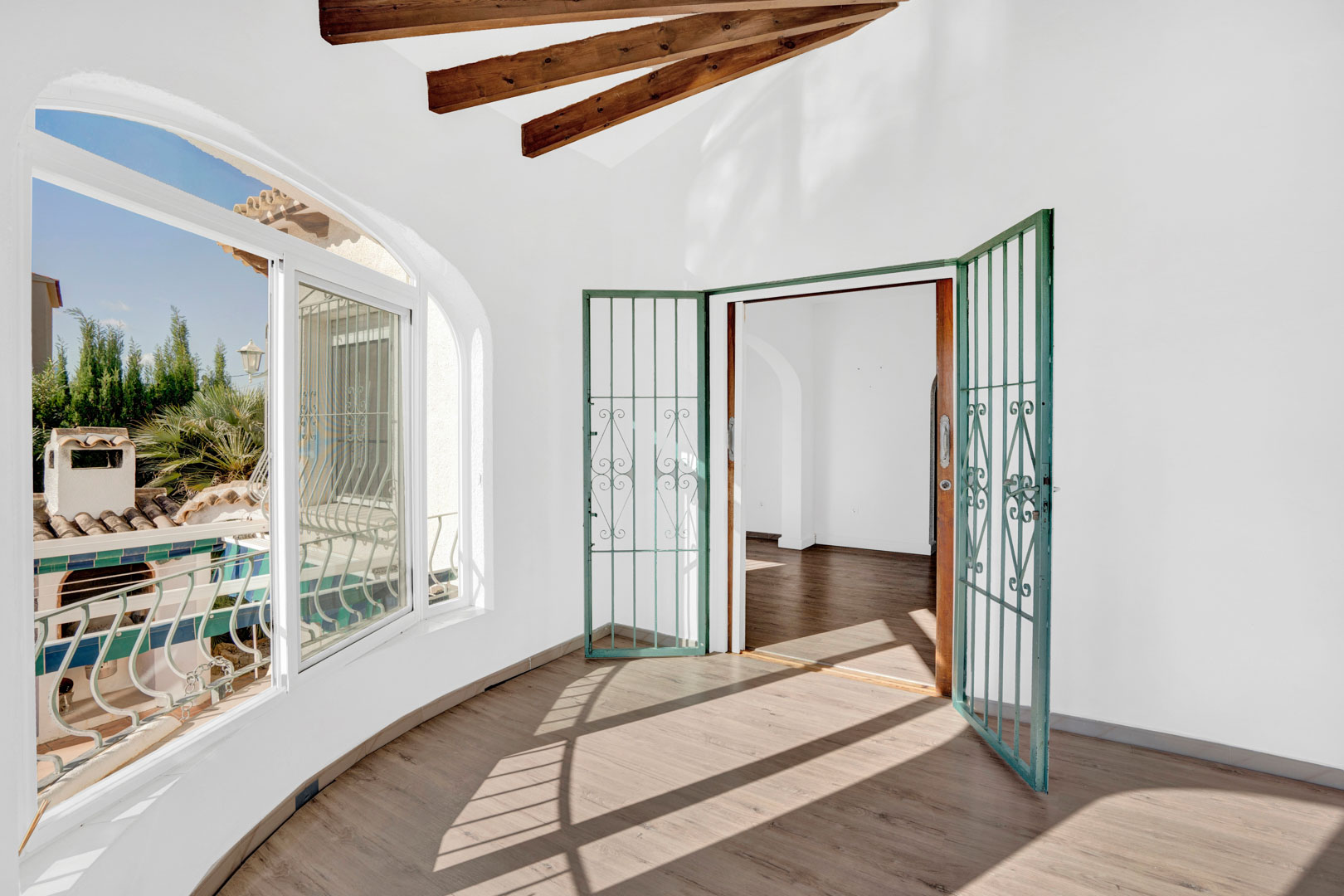 Glazed terrace featuring decorative wooden ceiling beams, wood-effect flooring, and large arched windows providing abundant natural light and garden views.