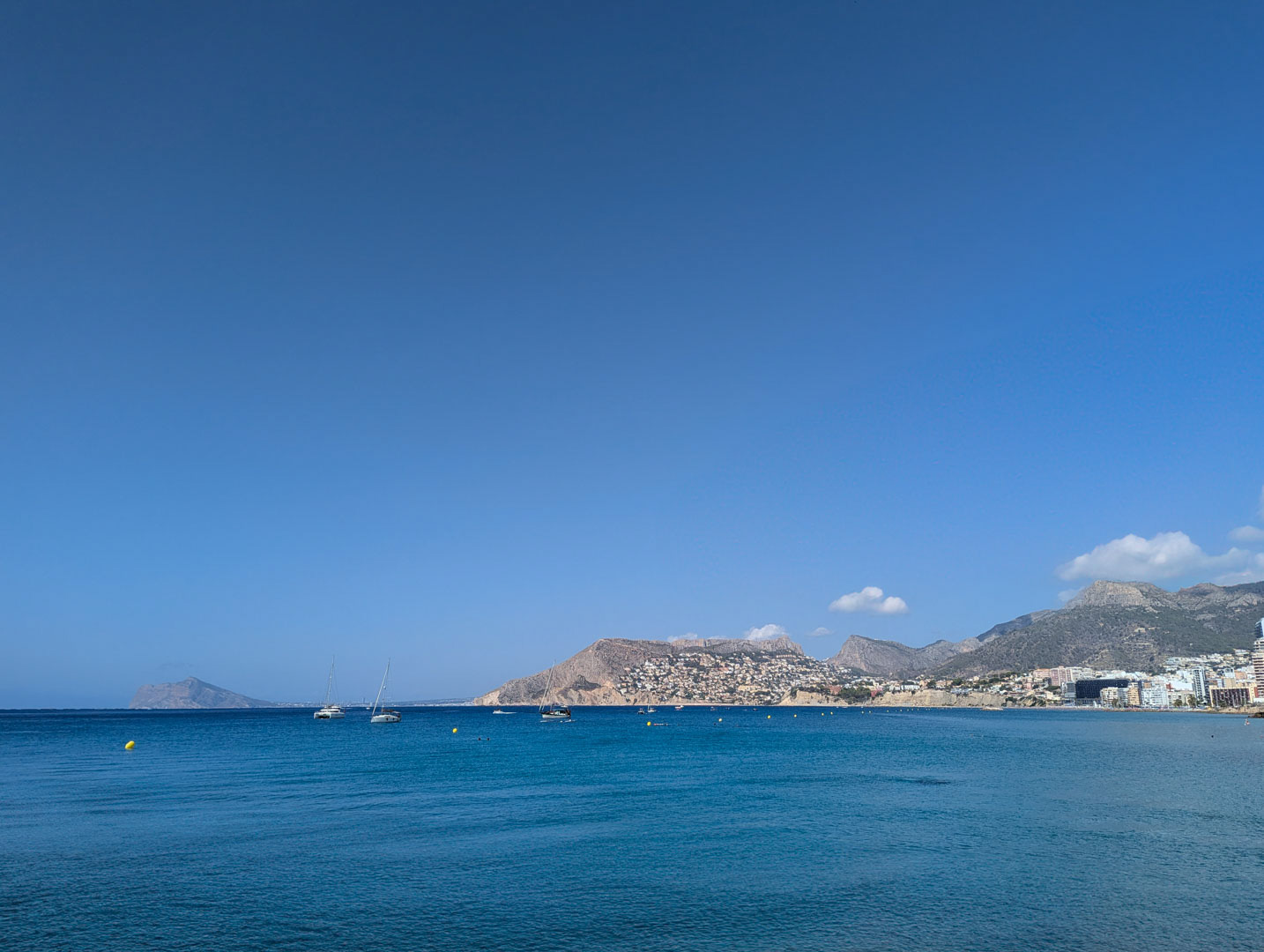Panoramic views of the Mediterranean Sea and the Calpe coastline featuring sailboats and distant mountains under a clear blue sky.