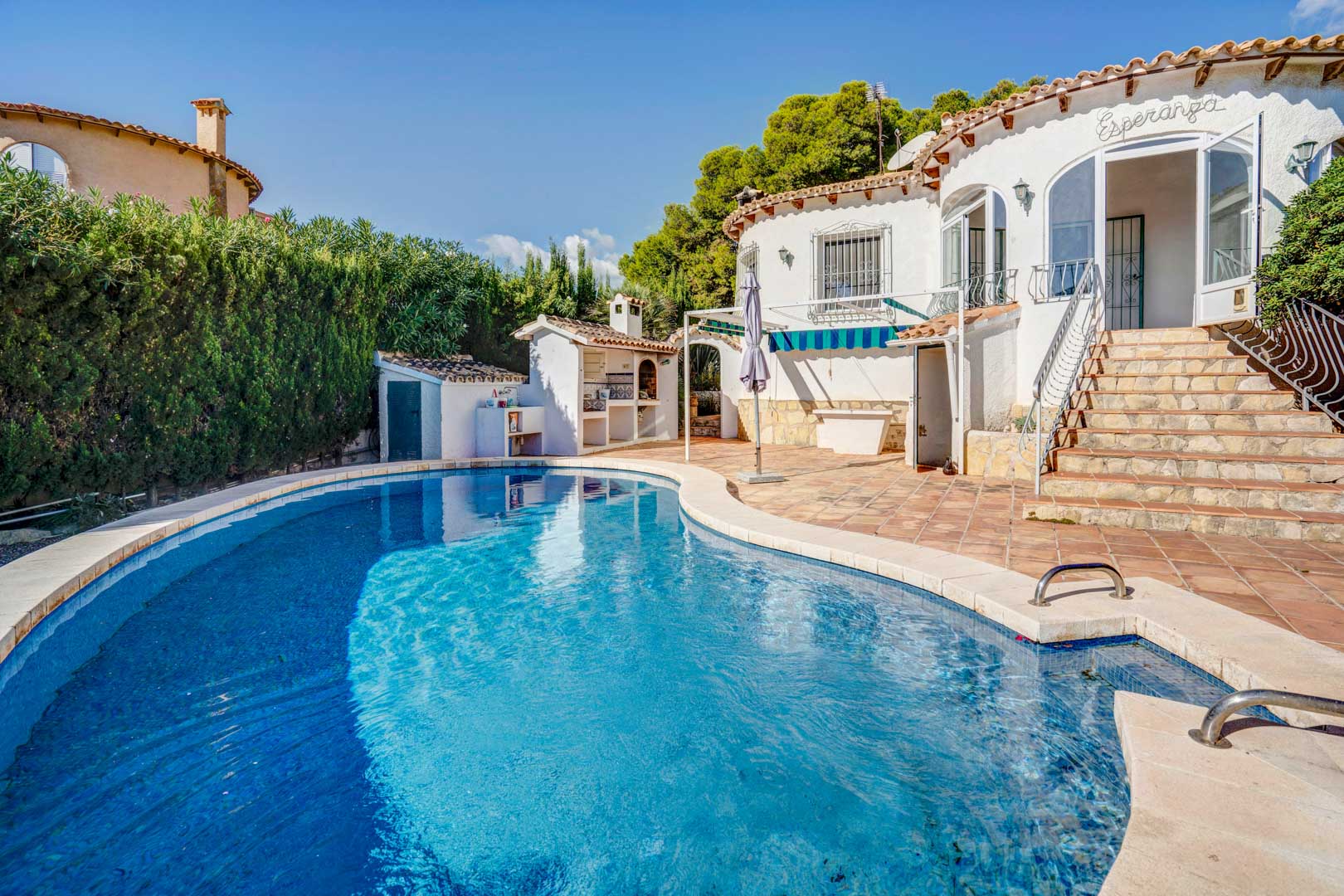 Private curved pool area featuring a terracotta tiled terrace, outdoor brick barbecue, and stone stairs leading to the main glazed entrance.