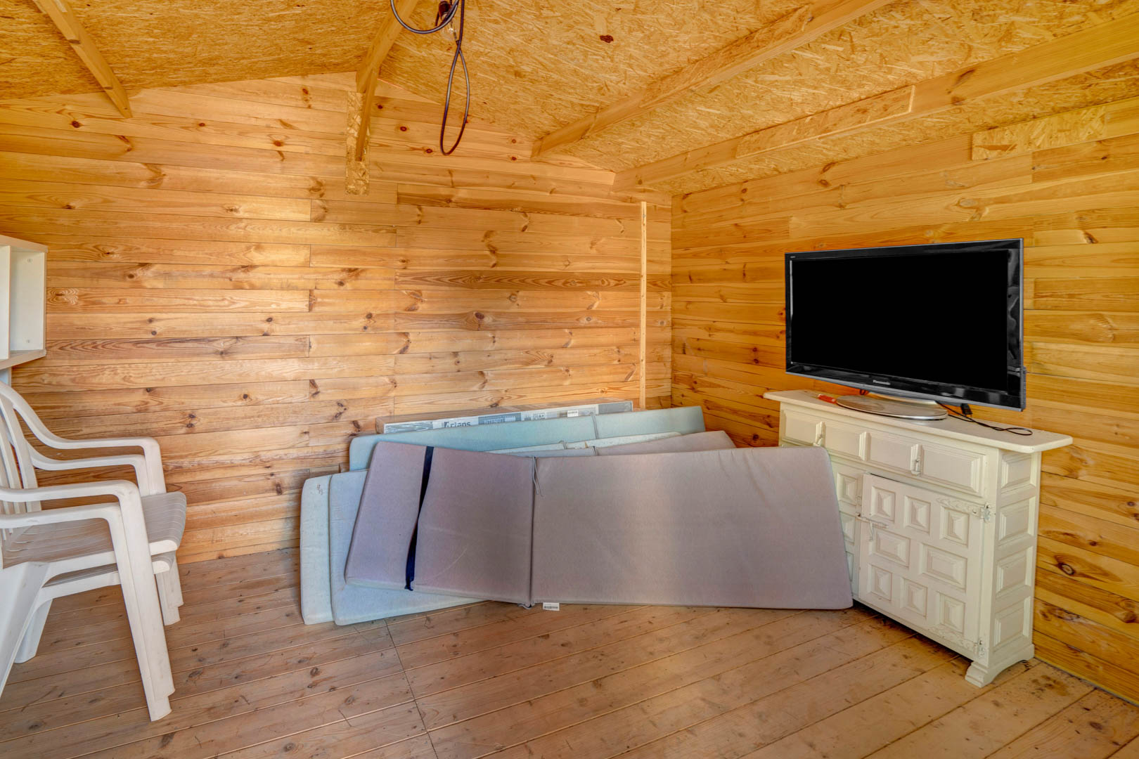 Wooden garden outbuilding or storage room featuring pine-paneled walls, a sideboard with television, and ample space for storing outdoor furniture cushions.