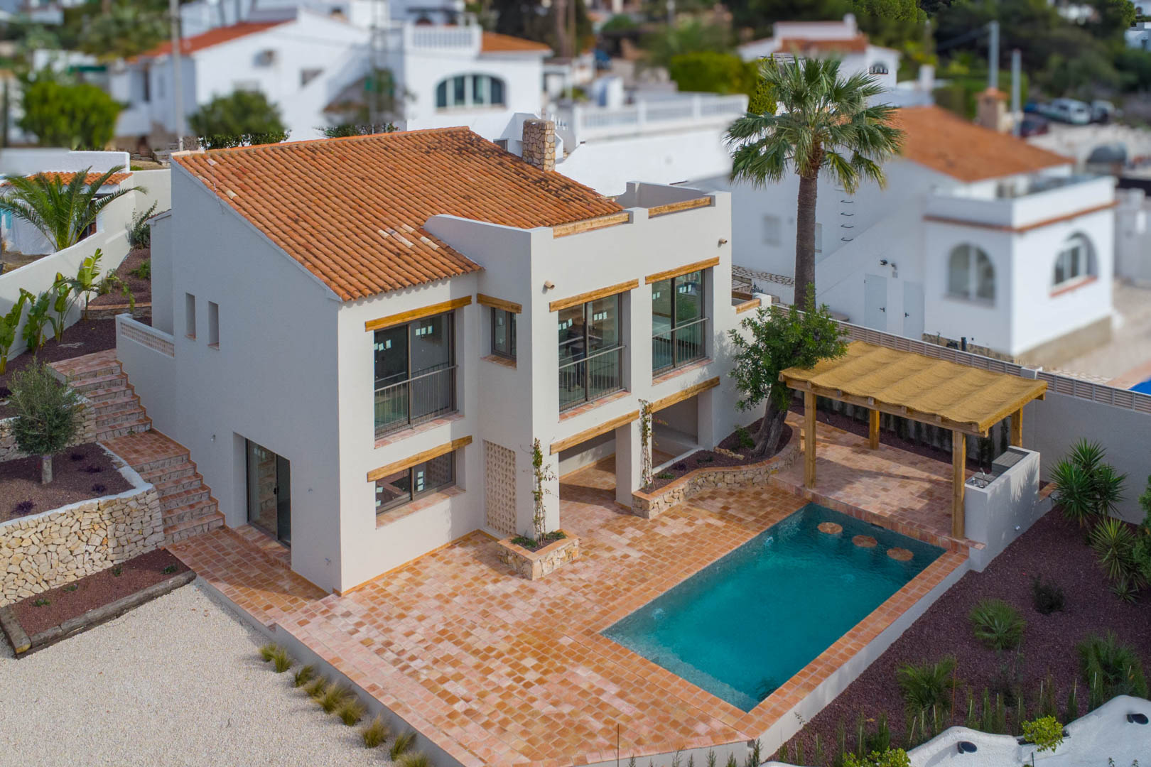Aerial view of the villa featuring a new swimming pool with submerged seating, terracotta tiling, and a wooden pergola with an outdoor kitchen area.