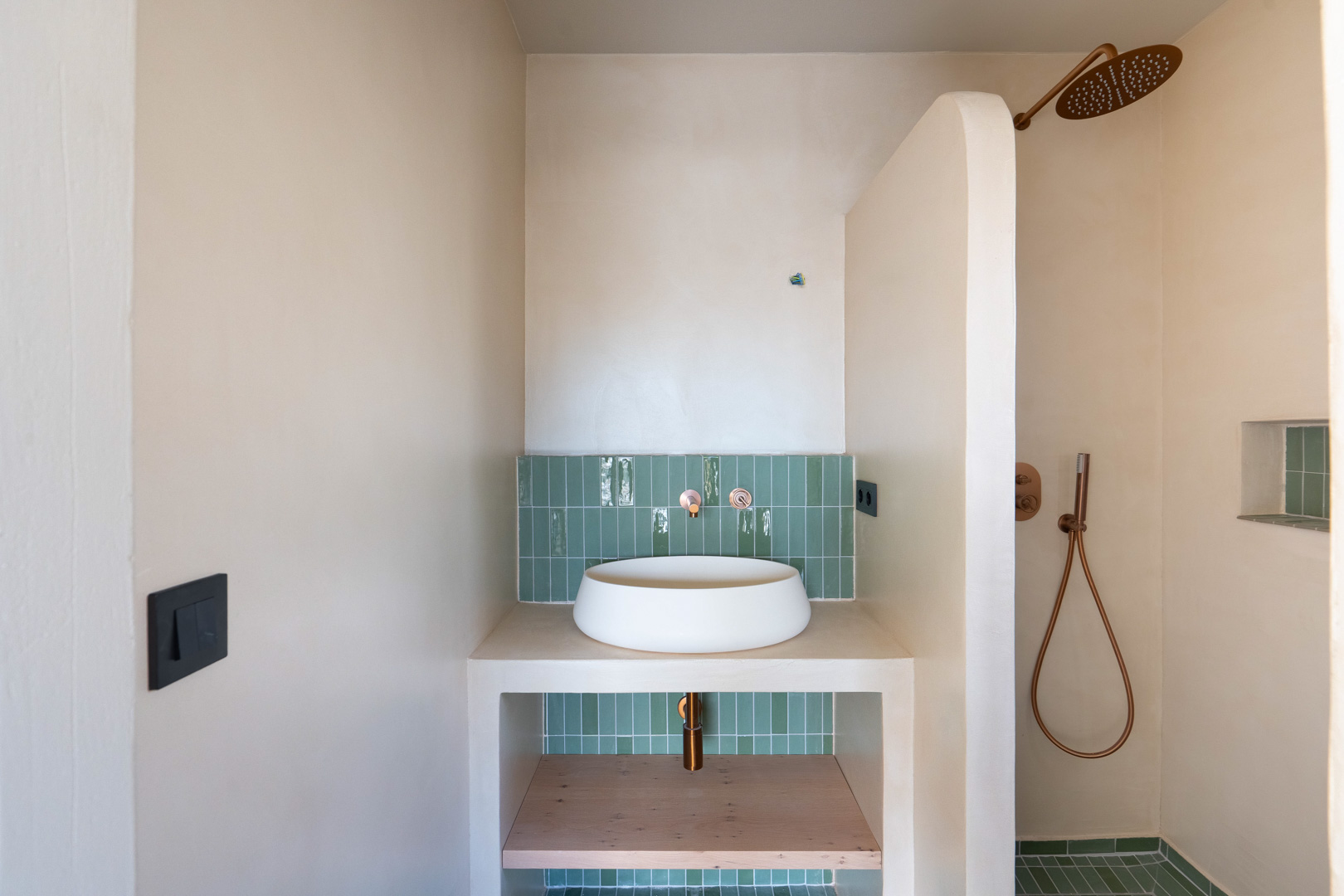 Bathroom featuring a vessel sink, copper fixtures, and green vertical tiling. Clay-finished walls and a walk-in shower with a unique curved partition wall.