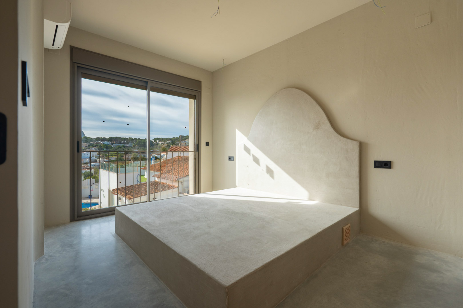 Bedroom featuring a built-in bed frame with a curved clay headboard, polished concrete flooring, and a sliding glass door opening to neighborhood views.