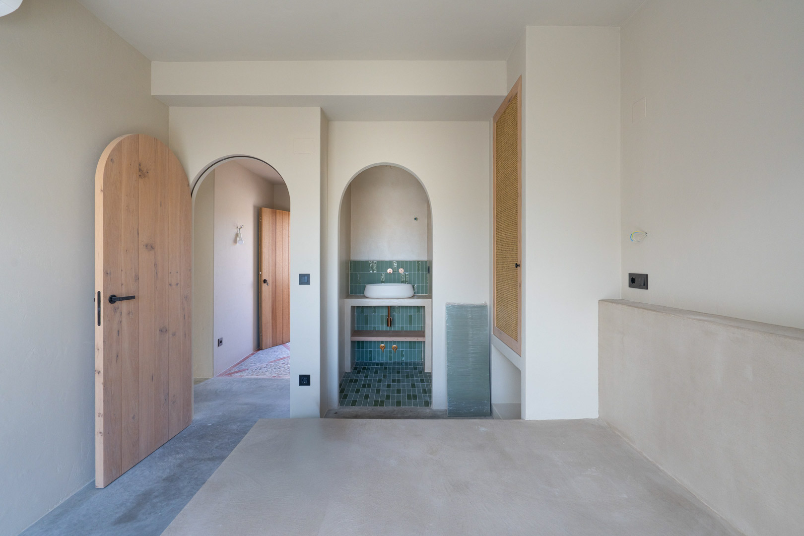 Bedroom featuring Matteo Brioni clay finishes, solid oak arched doors, and an integrated vanity nook with green tiling and polished concrete floors.