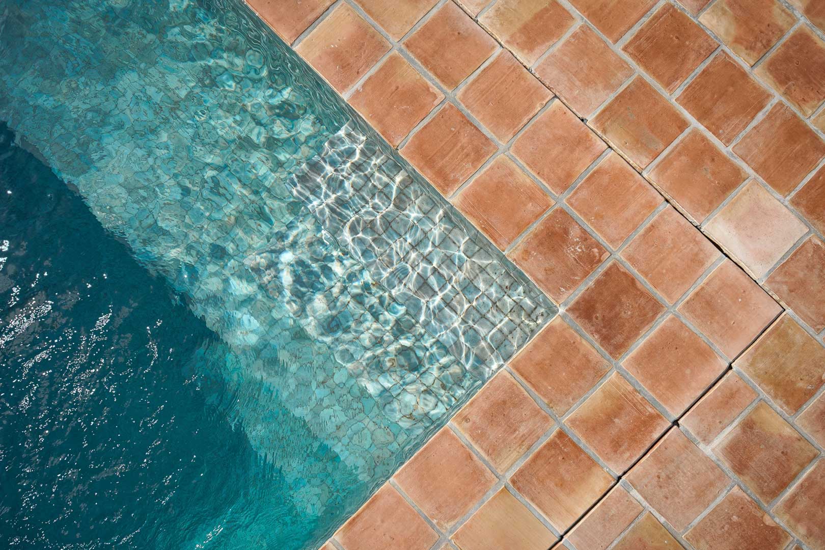 Close-up of the swimming pool corner featuring traditional terracotta tiles and clear turquoise water with natural sunlight reflections on the submerged steps.
