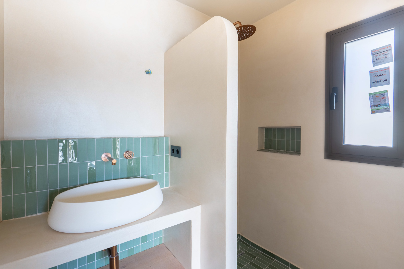 Designer bathroom featuring an oval vessel sink, copper wall-mounted fixtures, and vertical green tiling. Includes a walk-in shower with an integrated niche and clay finishes.